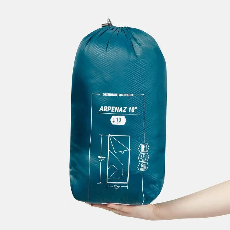 Blue sleeping bag in compression sack labeled "ARPEZ 10°" with specifications and dimensions, held by a person's hand.
