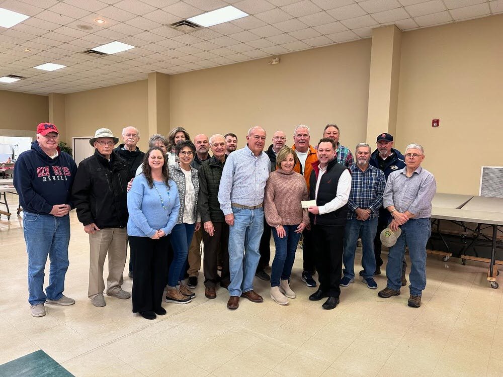 Group of people standing indoors, with one person handing a check to a woman in the center.