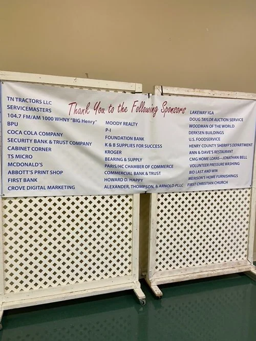 A banner thanking sponsors, listing various company names, in front of a white lattice fence.