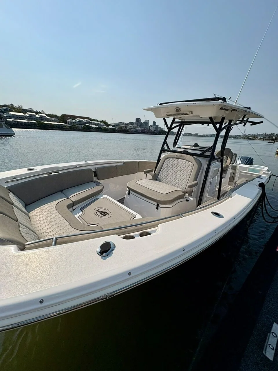 White motorboat docked on calm water with city skyline and houses in the background, clear sunny weather.