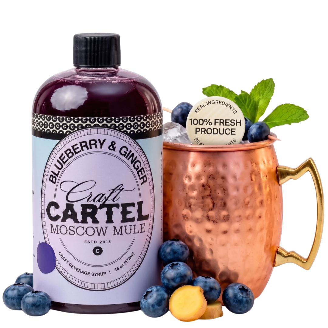 Bottle of blueberry and ginger Moscow mule craft beverage syrup next to a copper mug filled with ice, blueberries, and mint, with a label indicating 100% fresh produce.