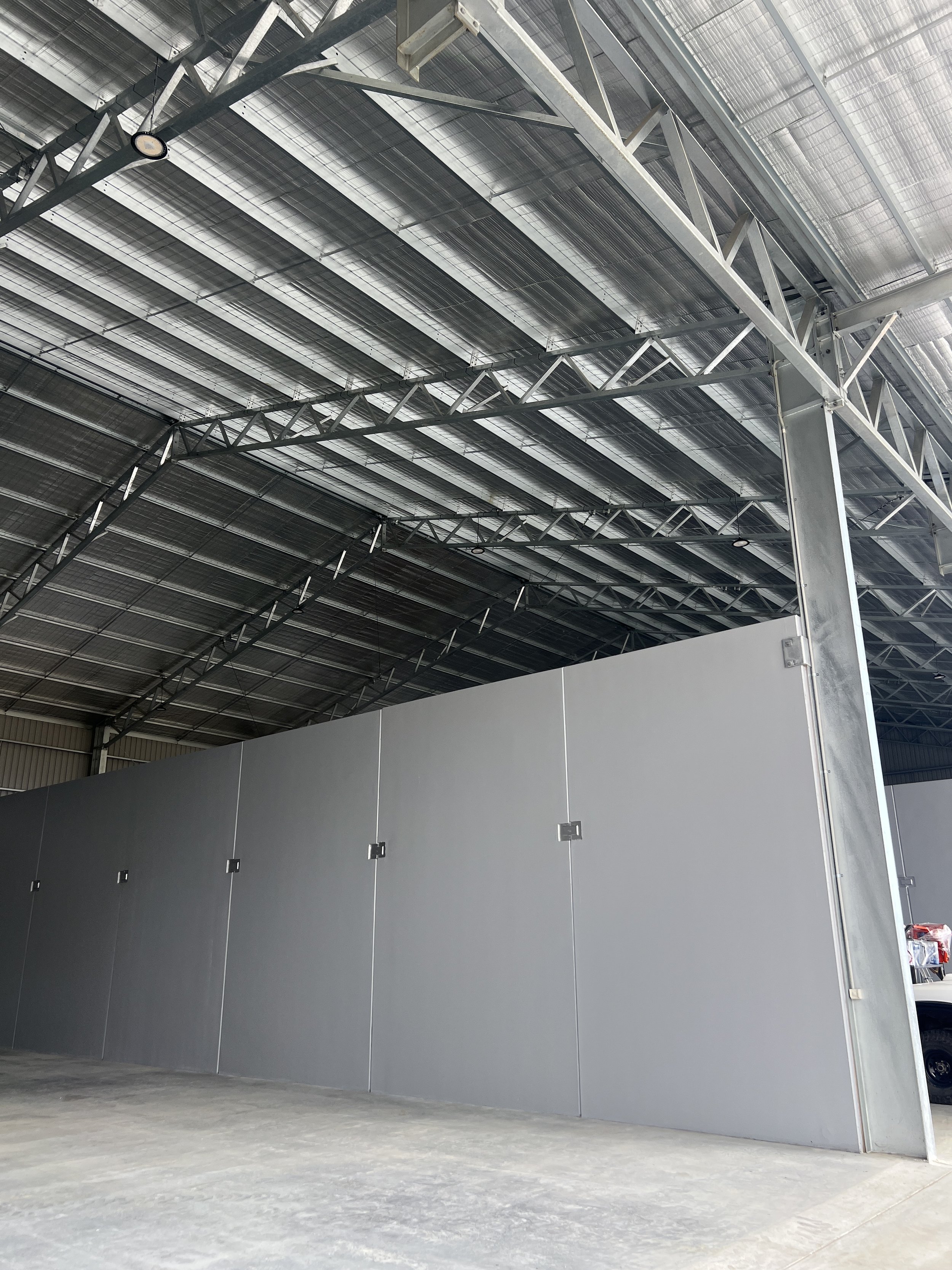 Interior of a warehouse with gray partition wall, metal roof, and steel support beams.