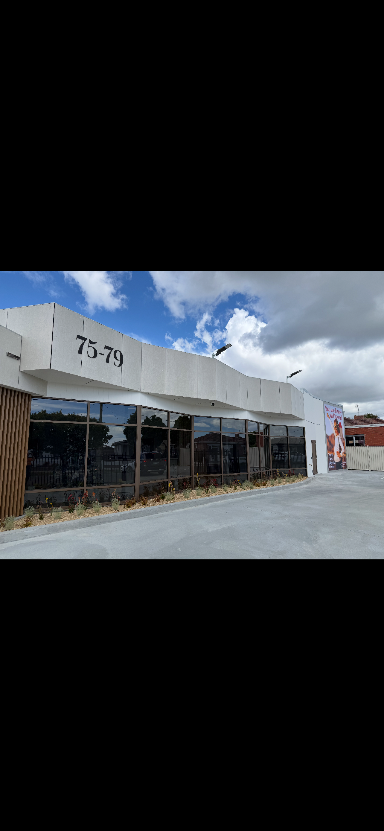 Modern commercial building with large glass windows, address 75-79, and a colorful billboard on the right side.
