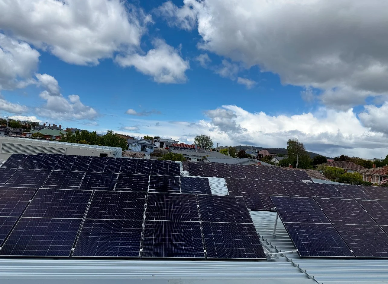 View of a rooftop covered with multiple solar panels against a partly cloudy sky and residential neighborhood.