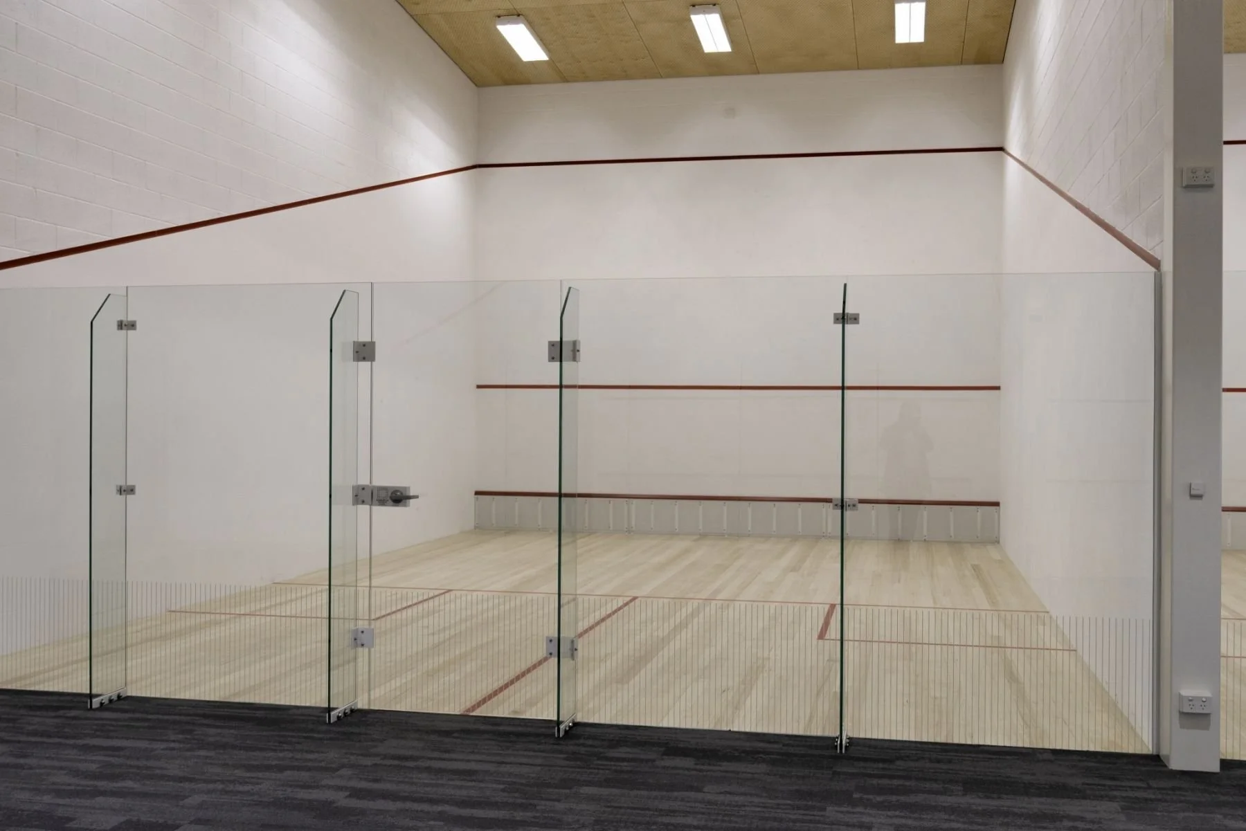 Empty indoor squash court with glass walls and wooden flooring.