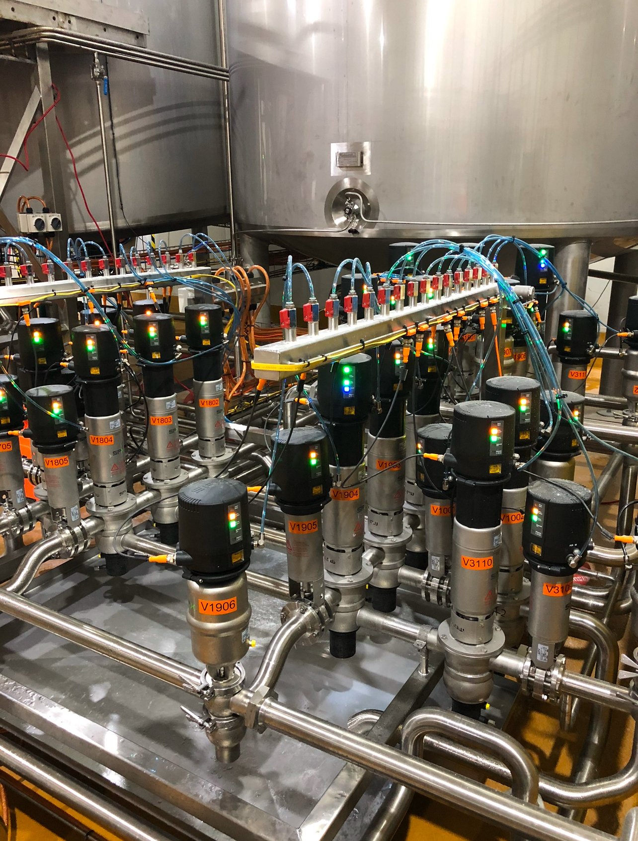 An industrial setup of metal pipes, gauges, and control valves with illuminated indicator lights in a manufacturing or processing plant.