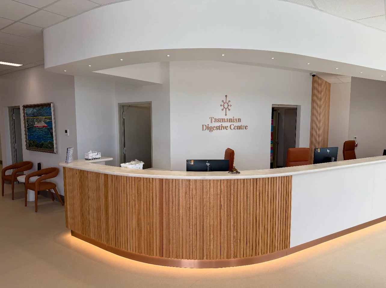 Reception area of Tasmanian Digestive Centre with a curved wooden front desk, three chairs on the left, and computer stations behind the desk.