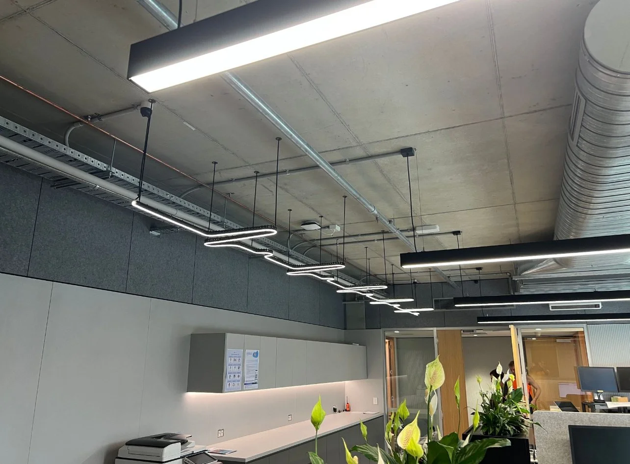 Modern office reception area with plants, gray cabinets, and bright lighting fixtures on a concrete ceiling with visible ductwork.