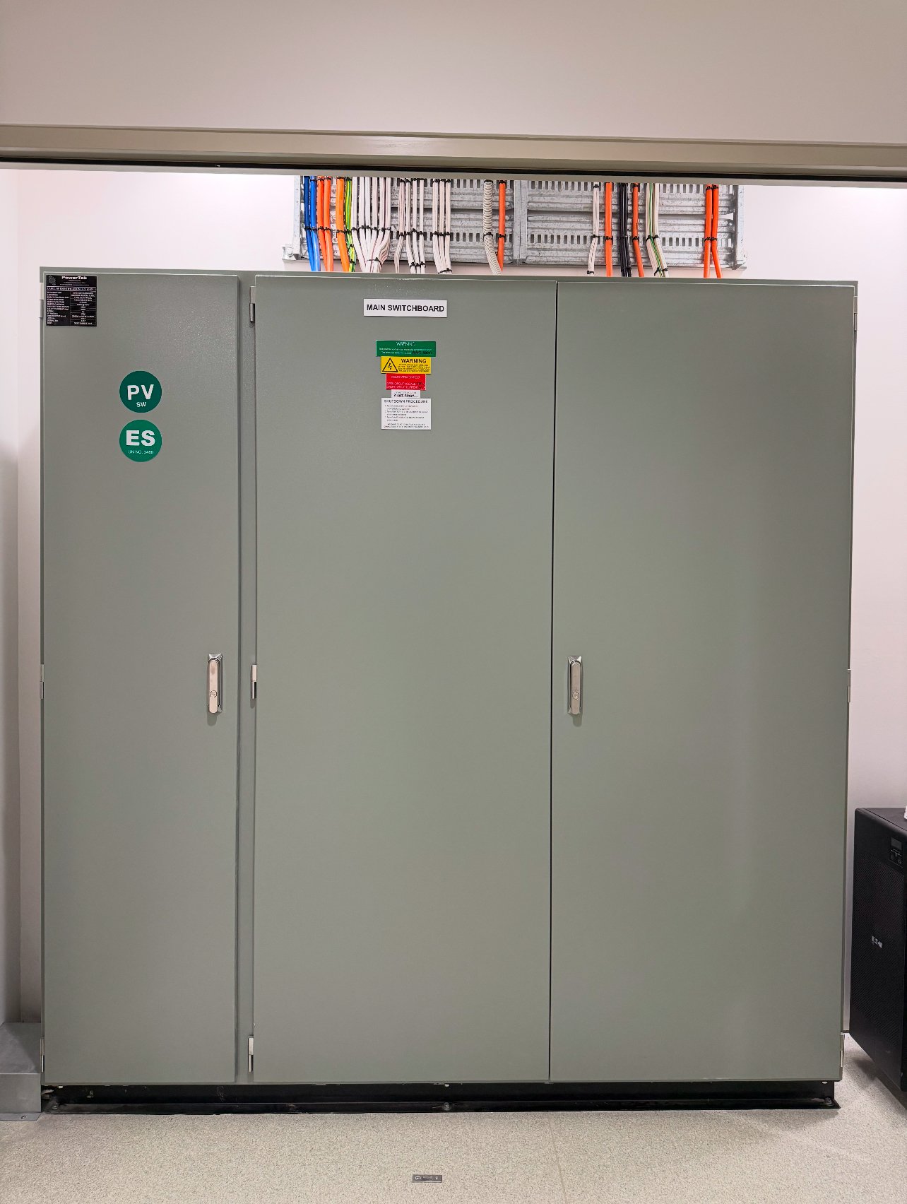 Electrical cabinet with labels, cables, and switches inside a building.