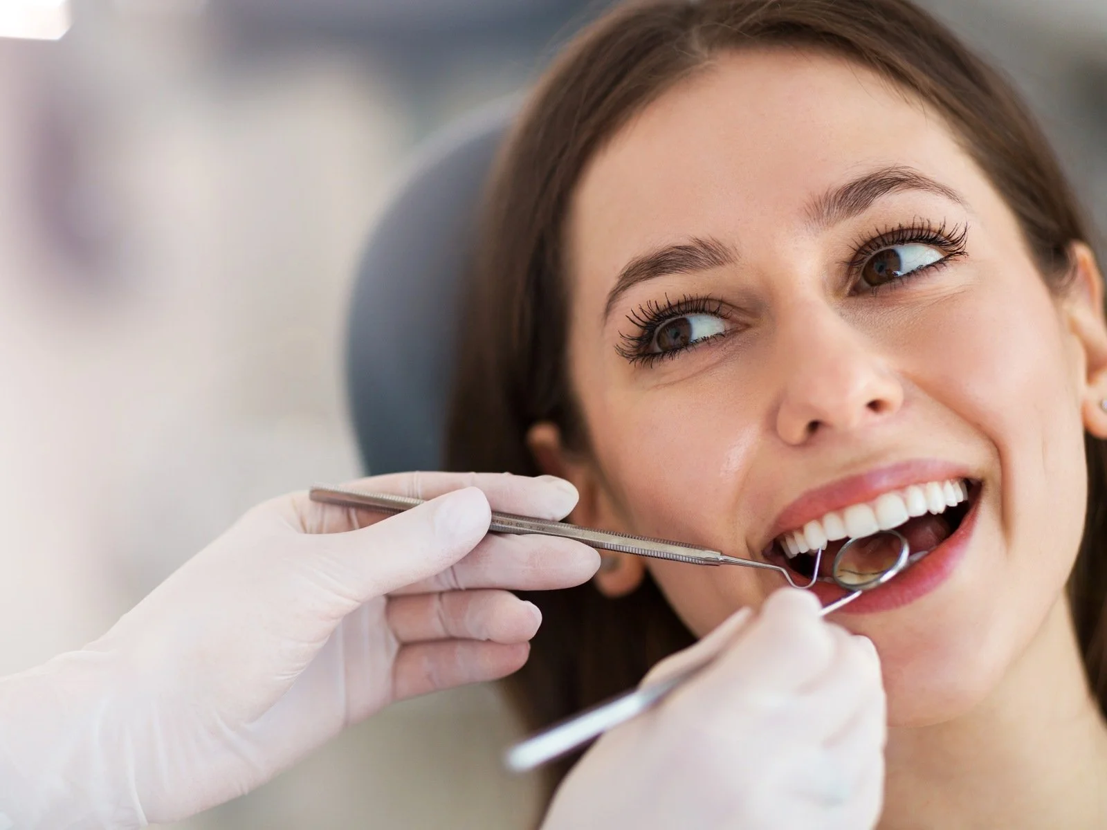 A woman at the dentist's office has her mouth open while the dentist uses dental tools to examine her teeth.