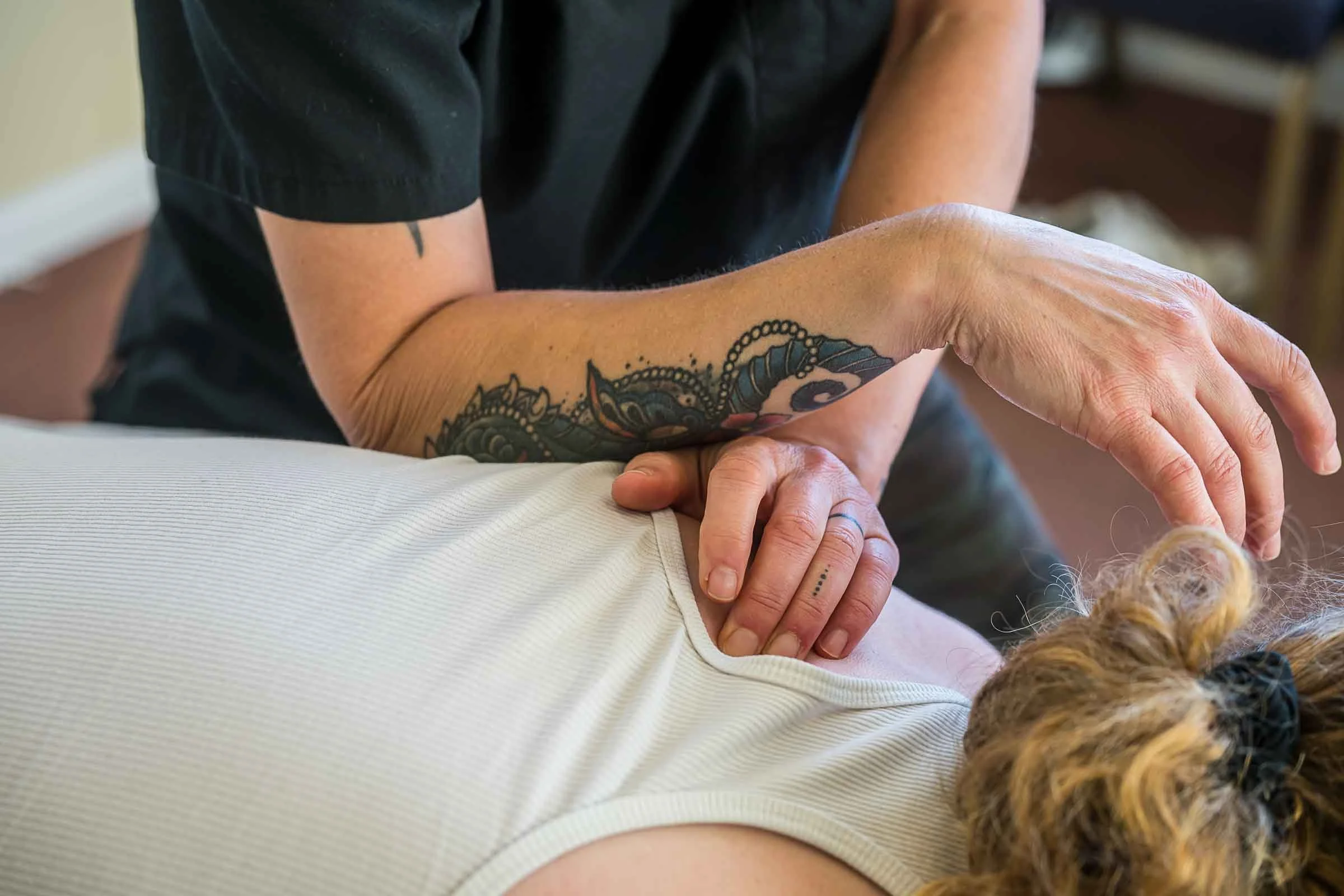 A person with a tattoo on their forearm receiving a massage from another person with curly hair.