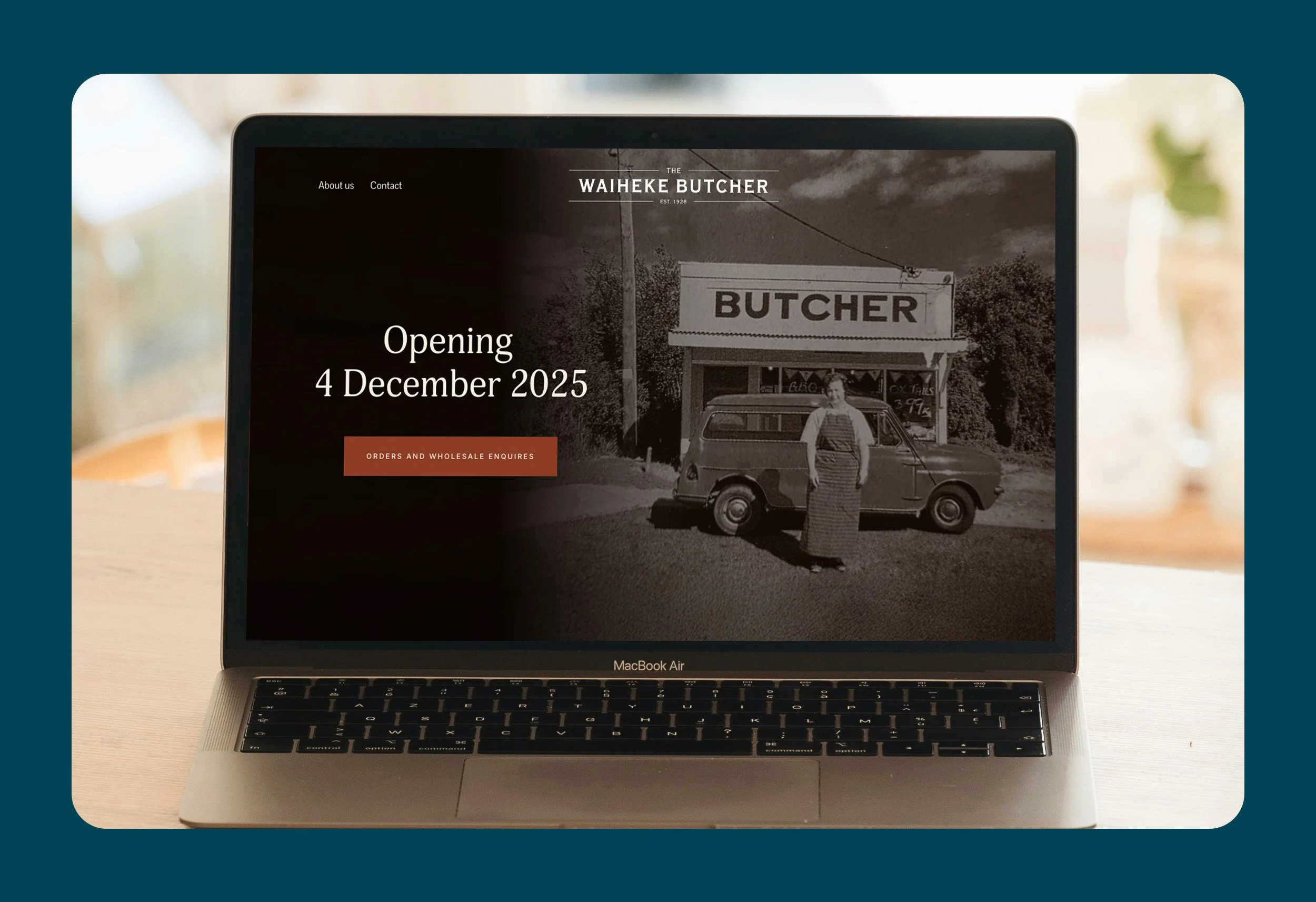Laptop displaying a website for the Waiheke Butcher, announcing the opening date of December 4, 2025, with an old black-and-white photo of a woman standing in front of a small butcher shop.