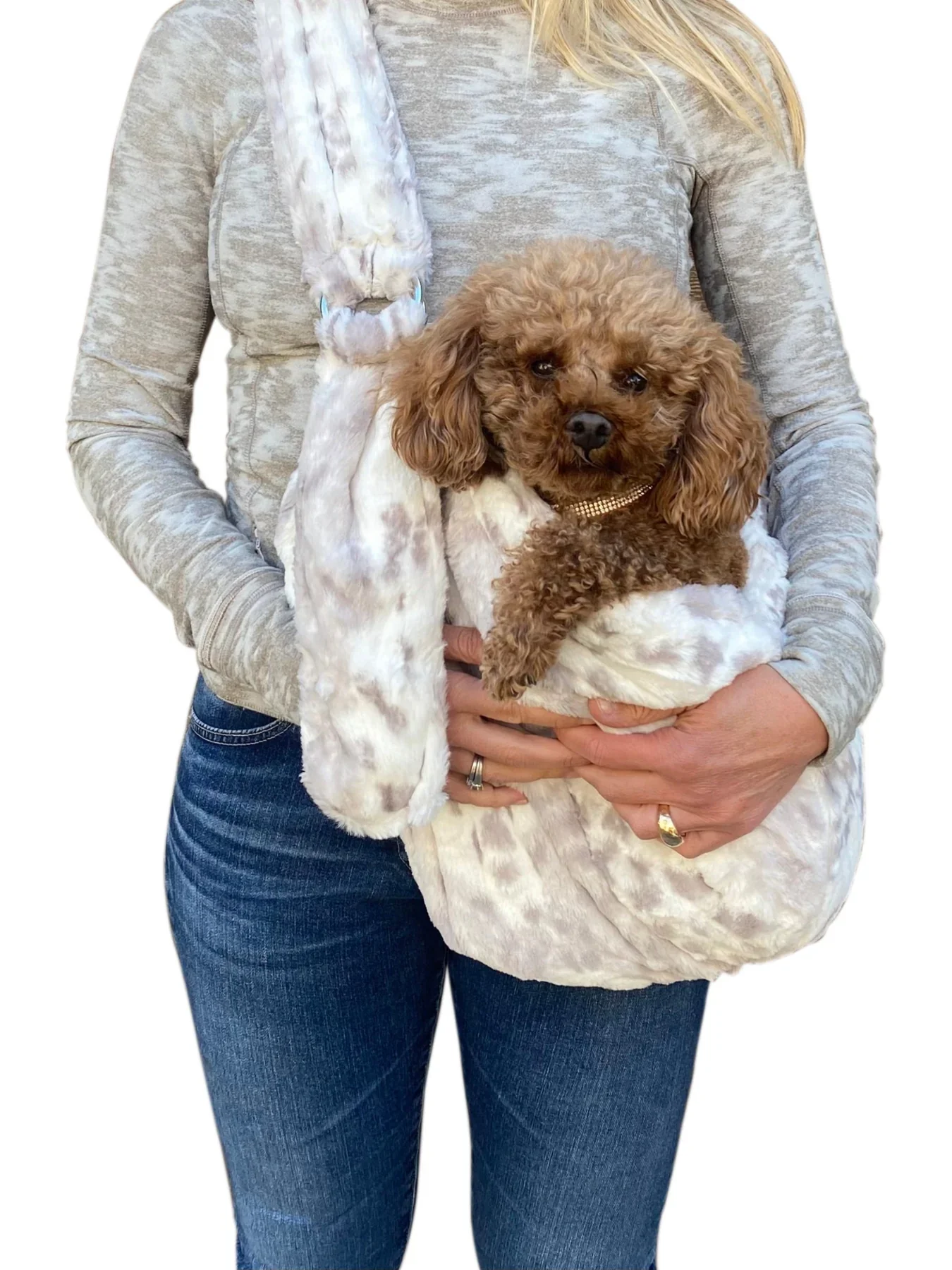Person holding a small brown poodle in a plush dog bed with a white and gray pattern, person wearing a gray long-sleeve top and blue jeans.