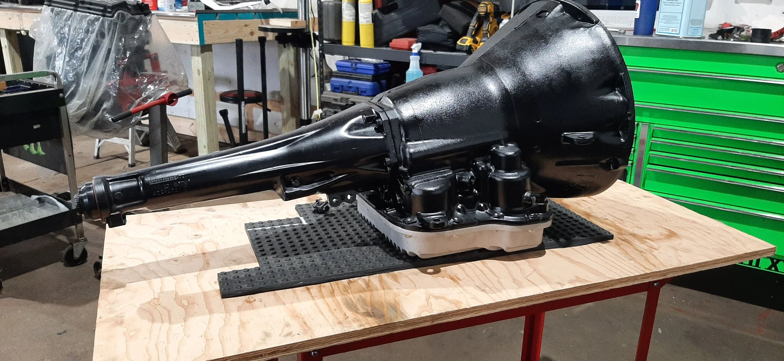 A large black automotive transmission placed on a wooden workbench in a workshop.