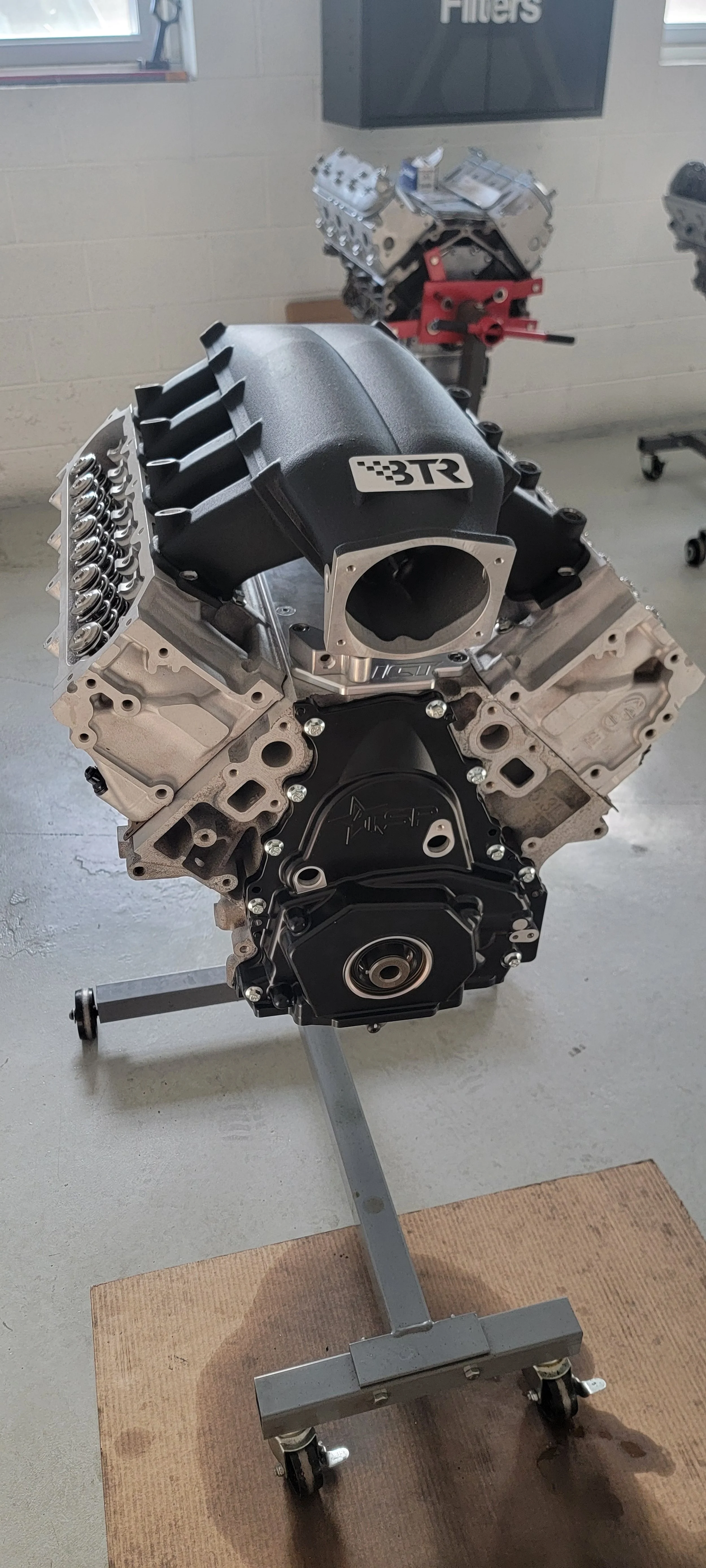A vehicle engine on a stand in a workshop, with a black 3TR sticker on the intake manifold.