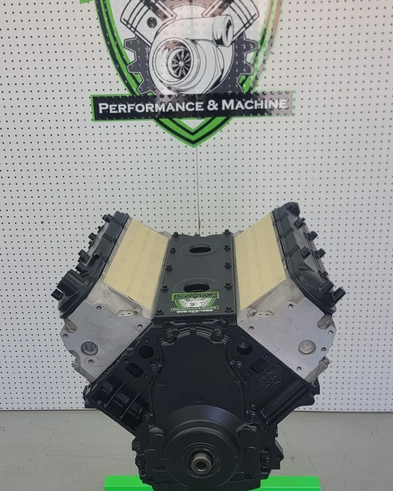 An automotive engine component displayed on a stand with a sign above that reads "Performance & Machine."
