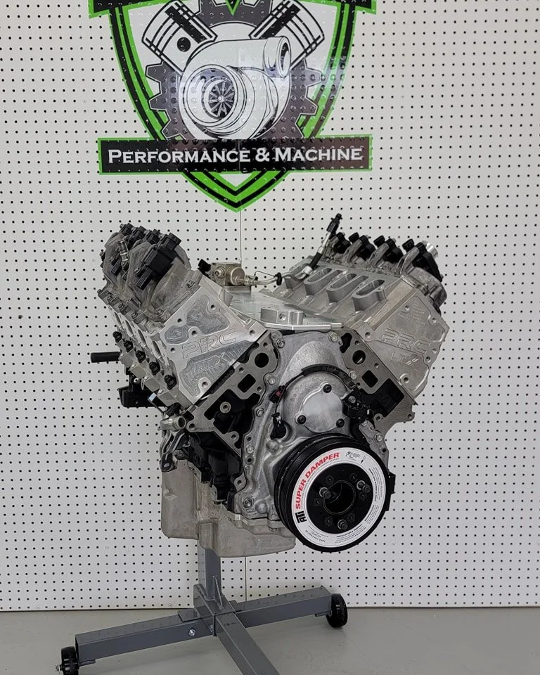 An automotive engine displayed in front of a performance and machine shop sign.