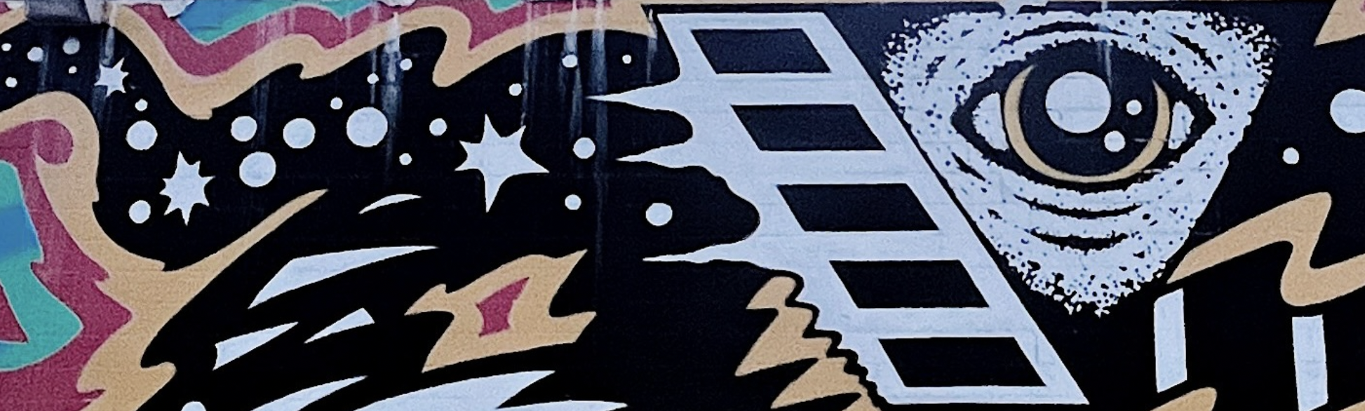 Modern building with wooden and metal exterior, large front window, situated in a mountainous landscape with grassy foreground and mountainous background.