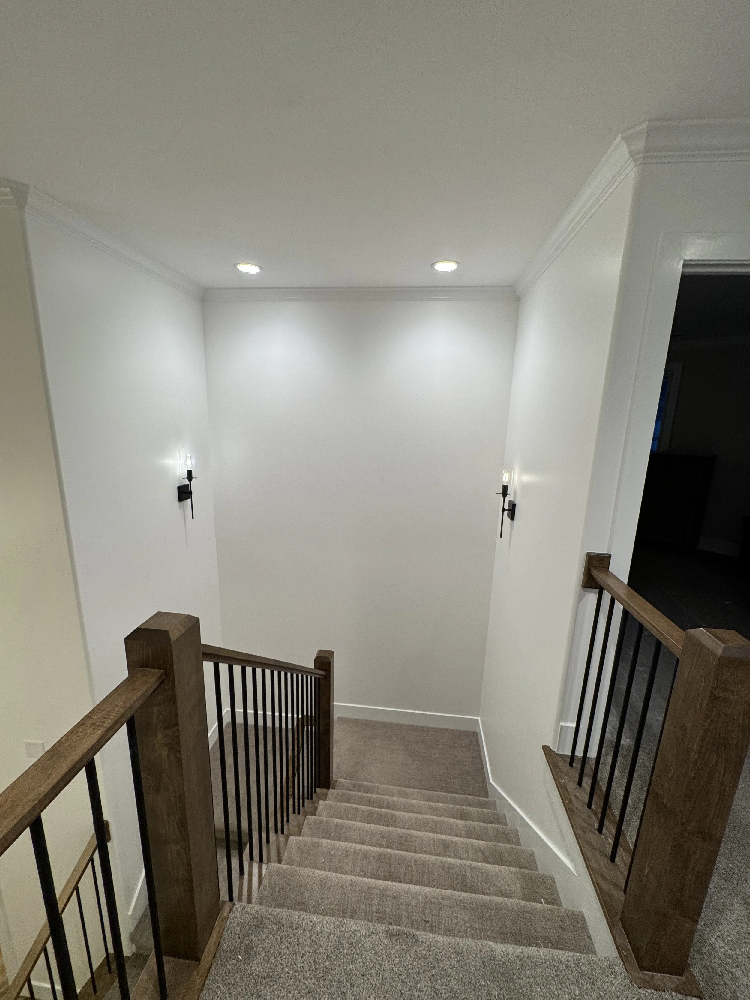 A staircase with recessed ceiling lights, and two modern wall sconces.