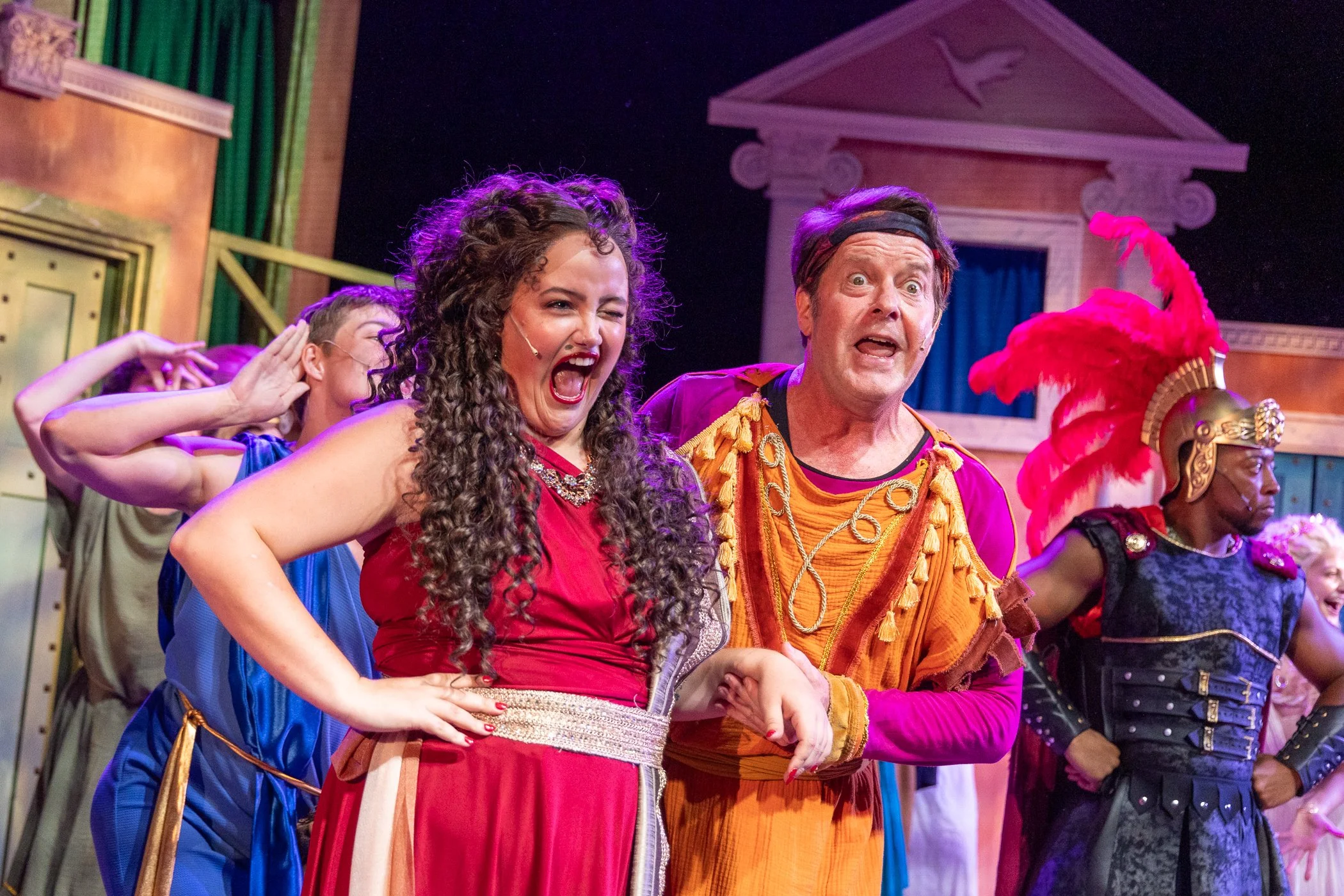 Actors performing on stage in a theatrical play, dressed in colorful costumes.