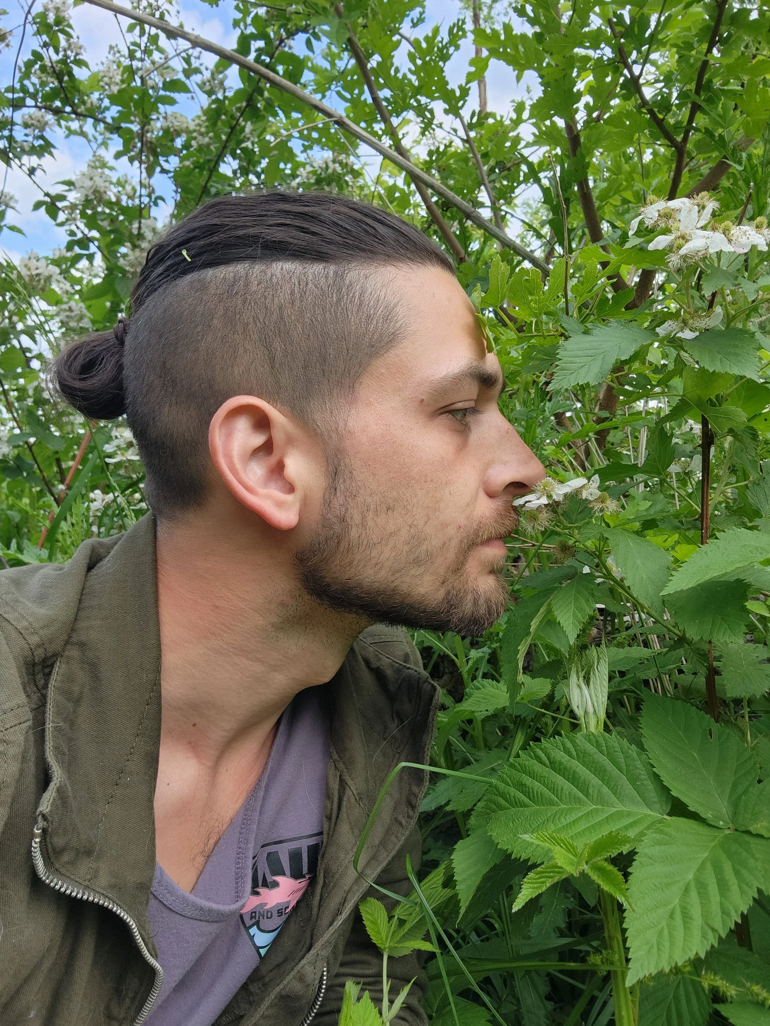 Side profile photo of a man interacting with nature and green leafy plants.