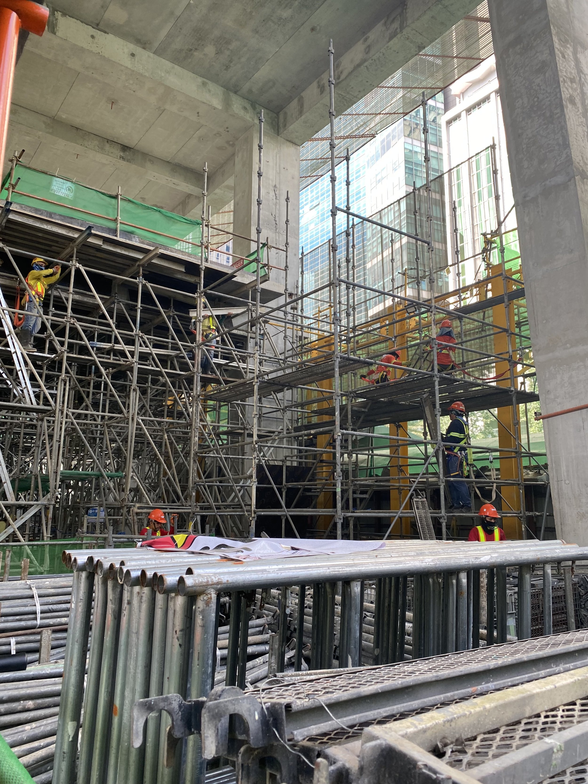 Construction workers wearing safety gear working on scaffolding at a building site in an urban area.