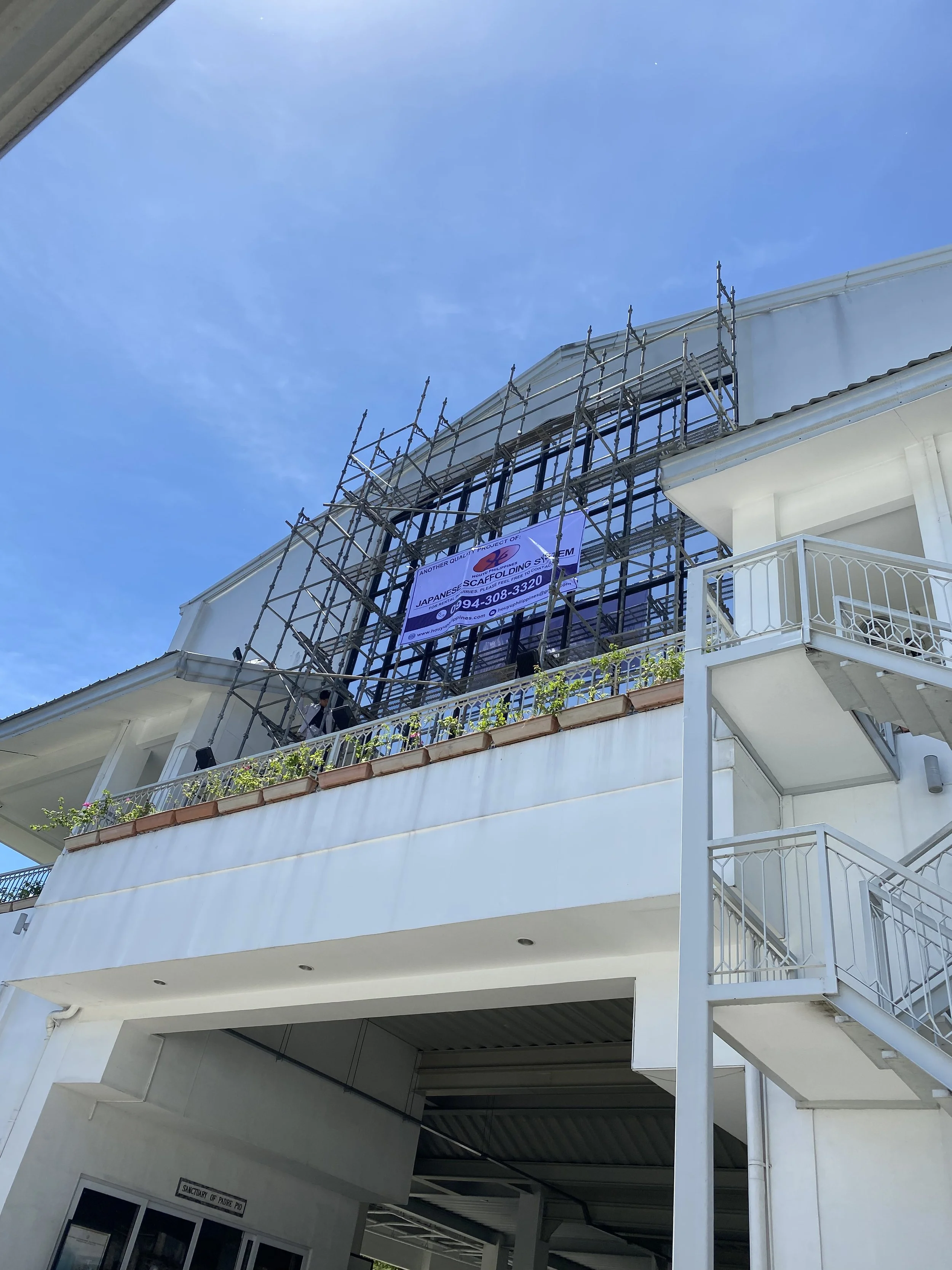 Building with scaffolding and a banner for Japanese scaffolding system, under a blue sky.