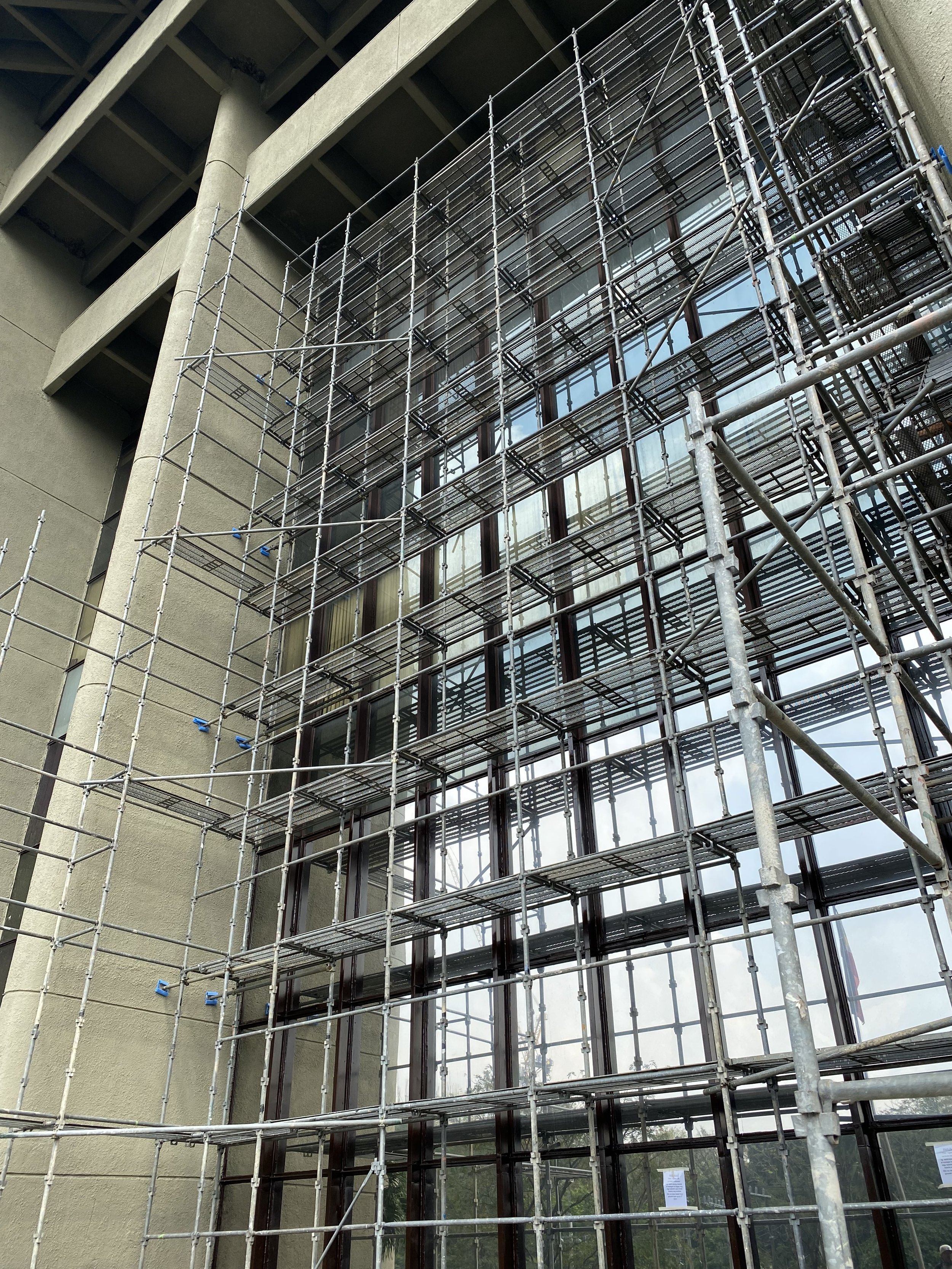 Construction scaffolding set up outside a building with large glass windows.