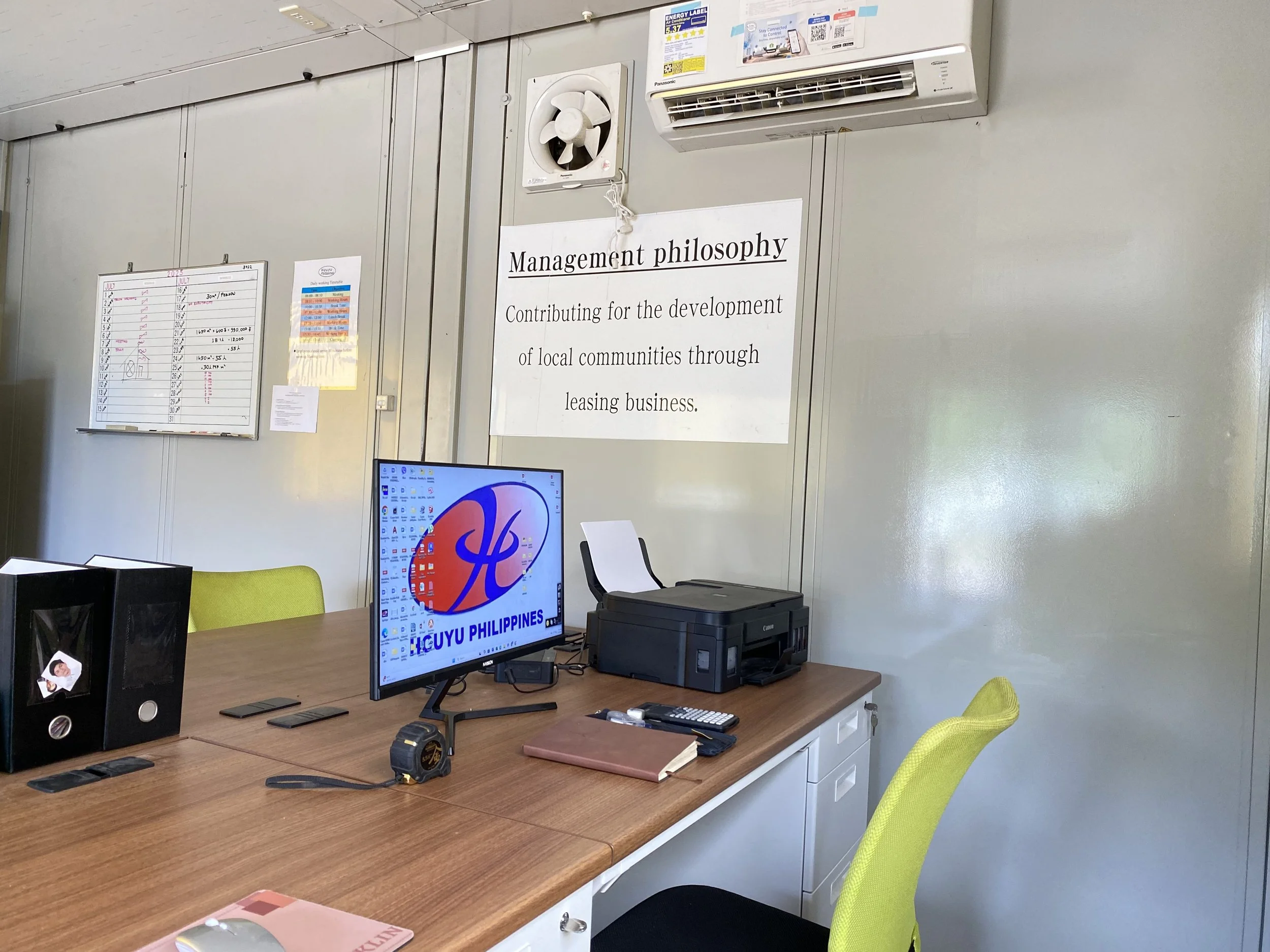 Office desk with a computer monitor, printer, books, remote control, and files, with Disney's logo and LIGUY Philippines on the screen, and a motivational management philosophy poster on the wall.