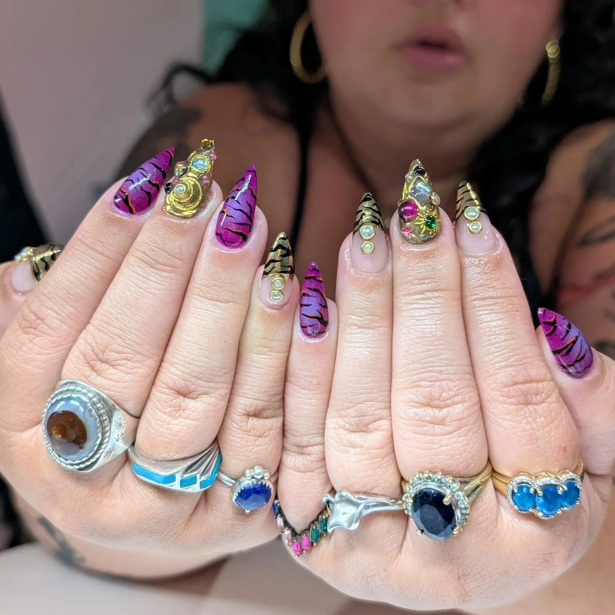 Close-up of a woman’s hands showing off colorful nail art and an assortment of rings, including silver, gold, and gemstone designs.