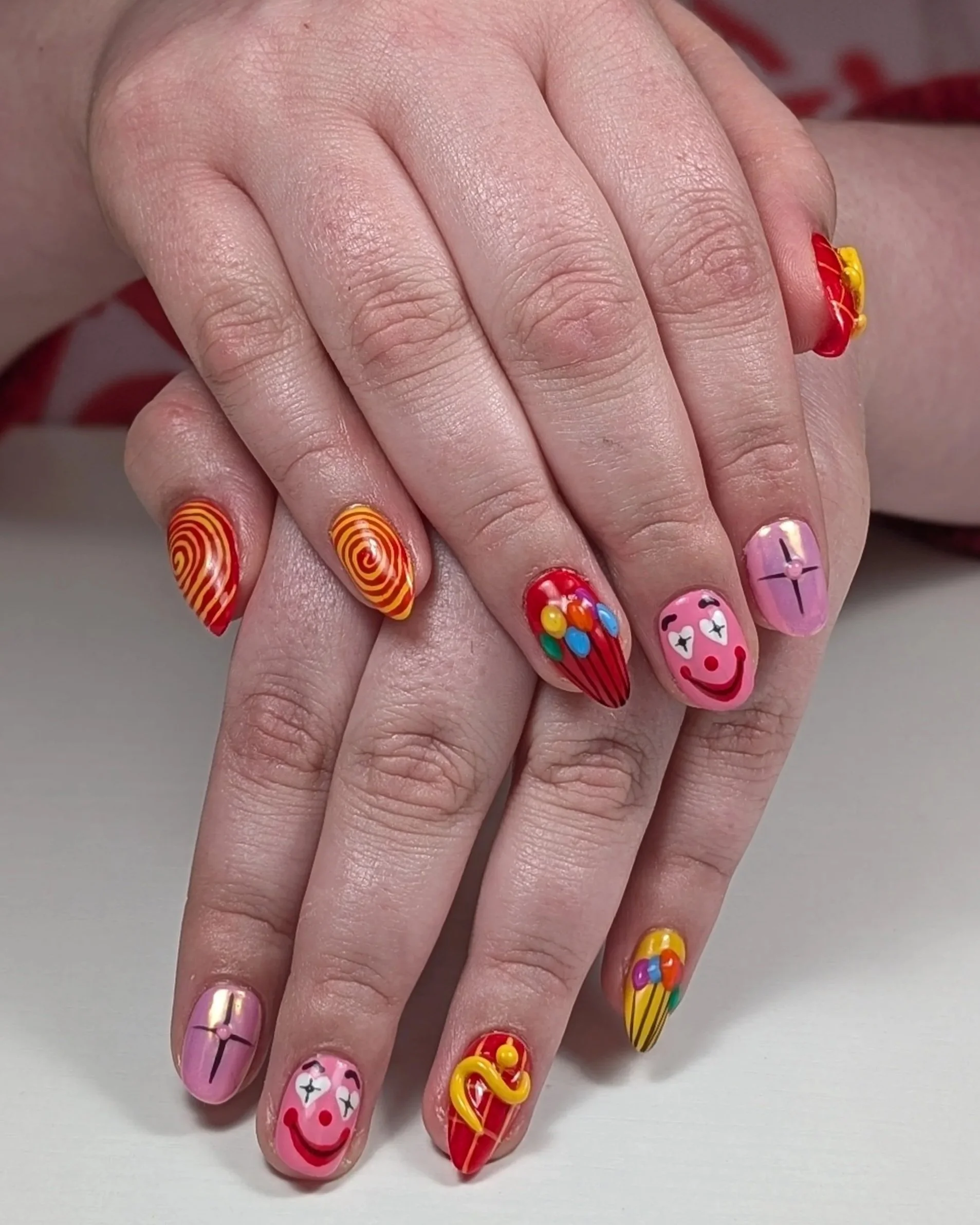 Hands with long nails featuring bright, multicolored nail art including swirls, dots, smiley faces, and raised decorative elements in pink, red, yellow, and blue.