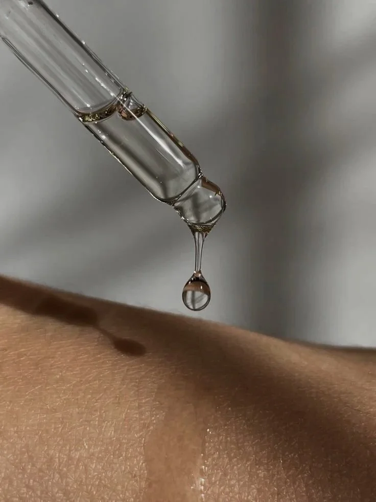 Close-up of a glass dropper releasing a droplet of liquid onto skin.