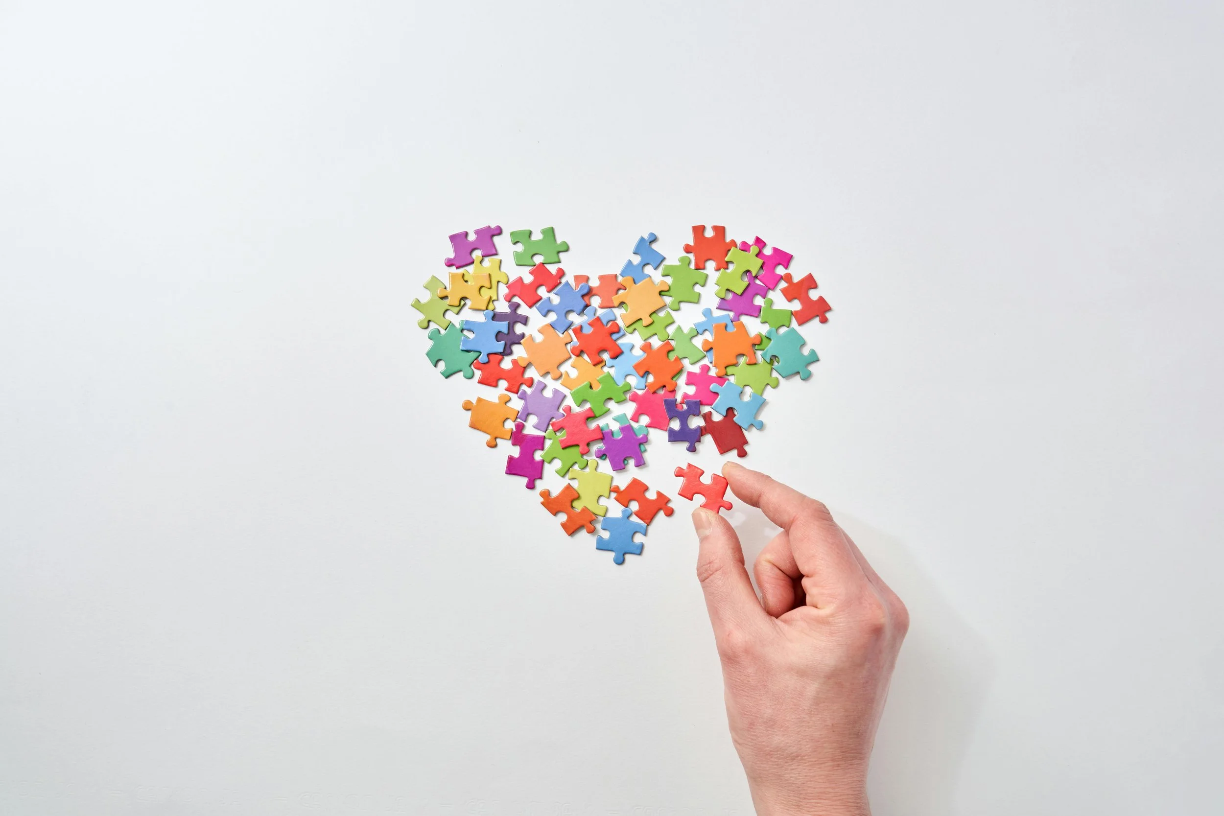 Colorful puzzle pieces forming a heart shape with a hand placing the final piece, symbolizing healing and making sense of grief and loss.