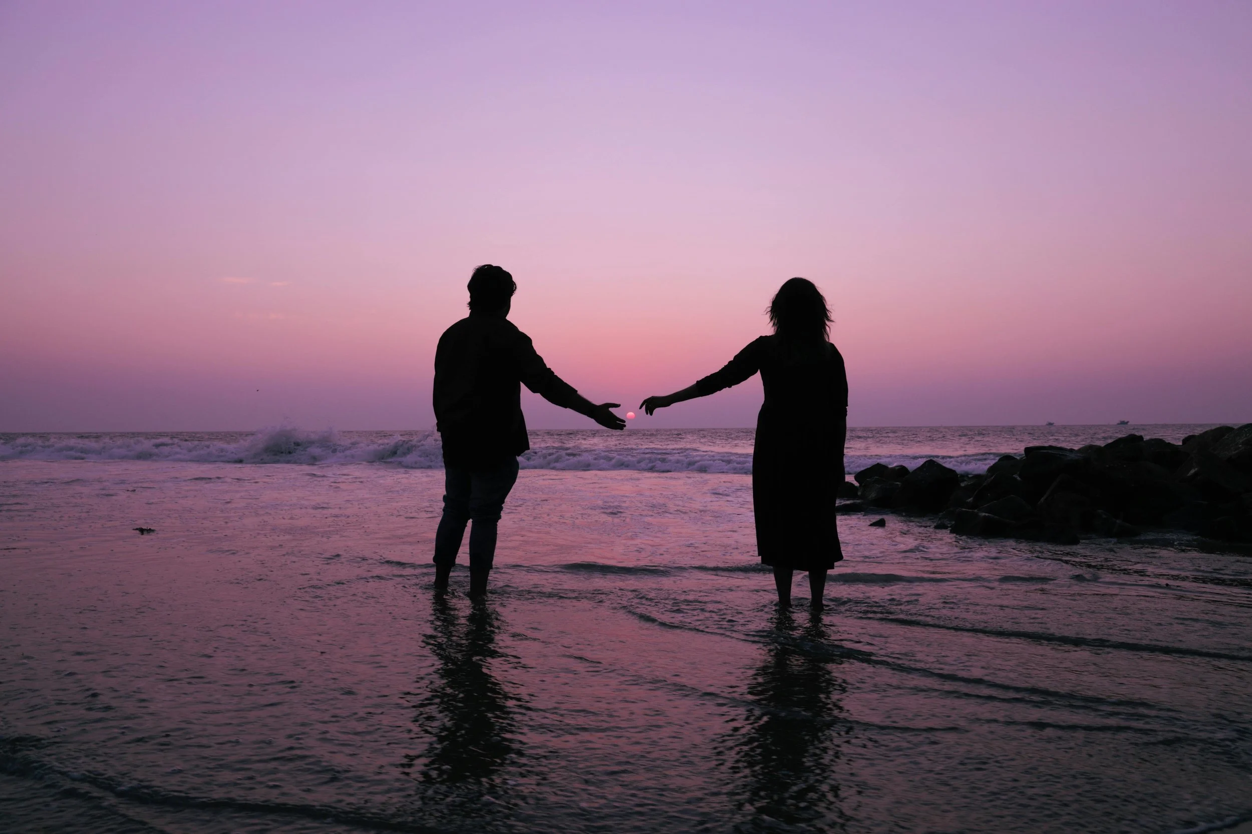 Couple holding hands at sunset in the ocean, symbolizing reconnection and support in couples therapy.
