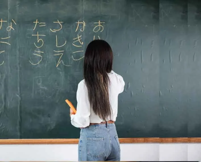 A girl writing Japanese characters on a chalkboard in a classroom.
