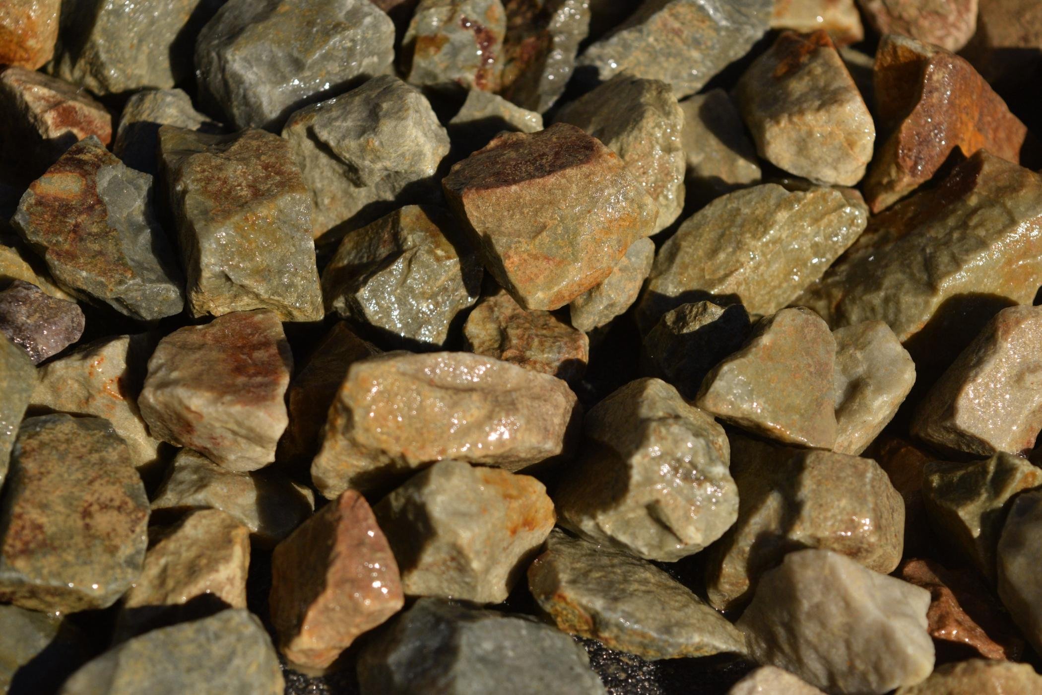 Close-up of small, irregularly shaped rocks and stones with wet appearance, varying in color from gray to reddish-brown.