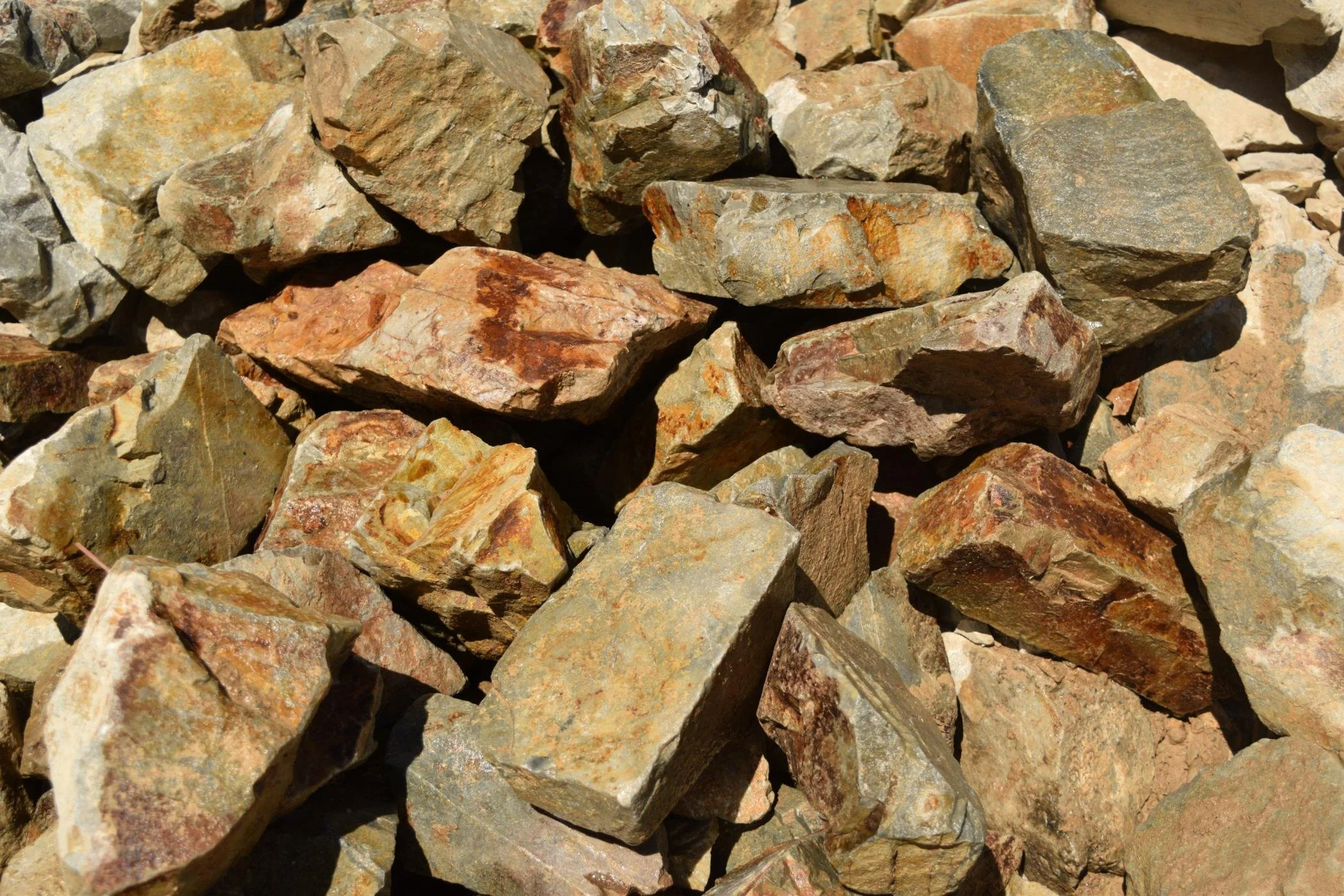 Close-up view of various irregularly shaped rocks with a mix of beige, reddish, gray, and brown shades.