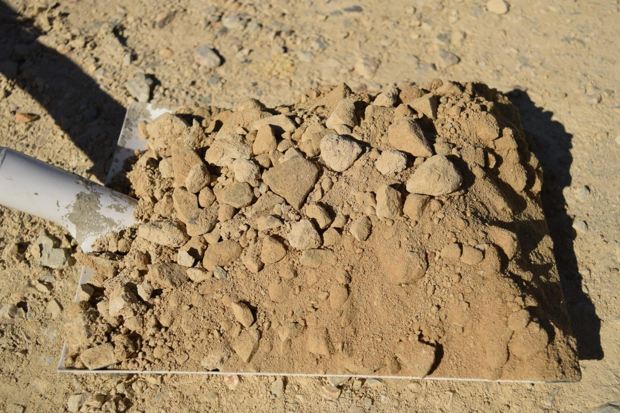 Pile of small rocks and dirt on a sandy ground with a white pole on the left side.