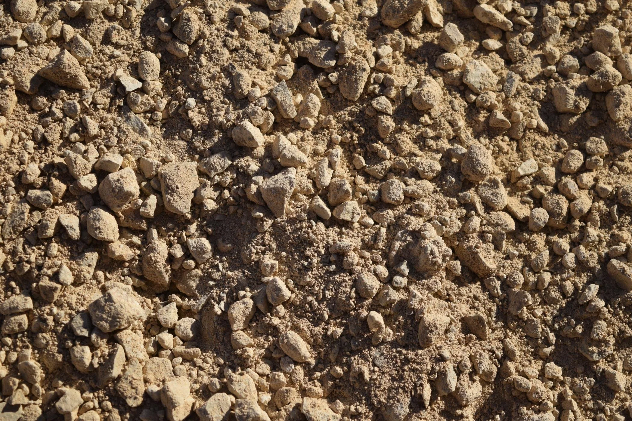 Close-up view of coarse, light brown gravel with various-sized rocks.