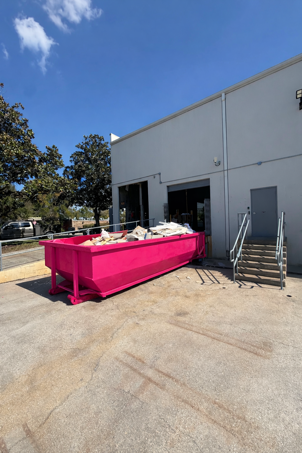 Large pink dumpster filled with cardboard and paper outside a white industrial building under a blue sky.