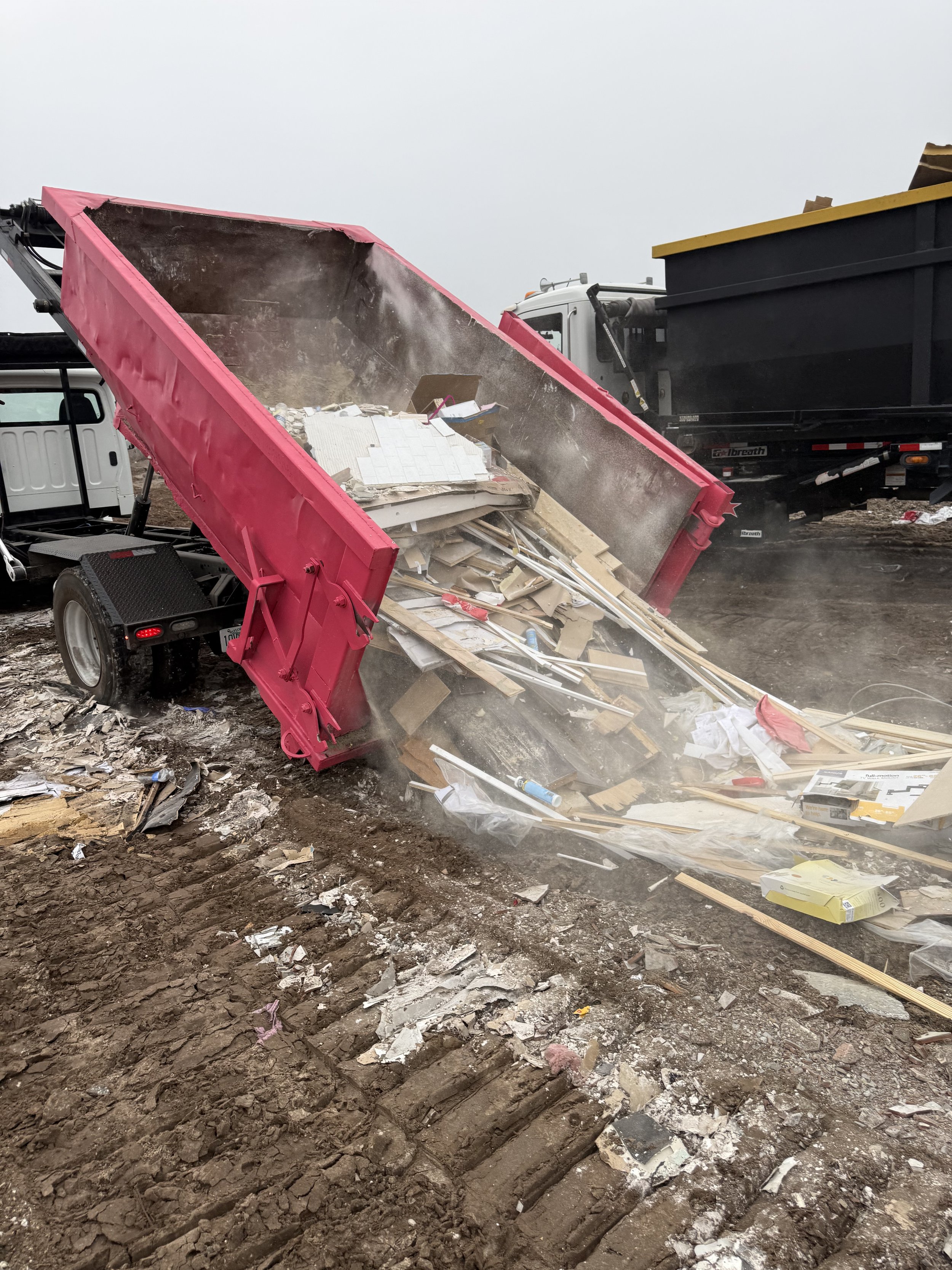 A pink dump truck unloading debris onto a dirt ground at a construction site with other vehicles and equipment nearby.