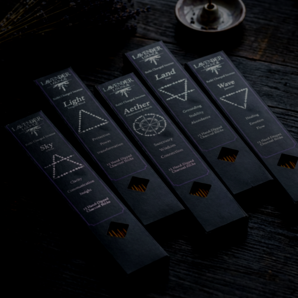 A box of lavender incense sticks surrounded by small, colorful stones or crystals on black fabric with white paisley patterns, and a metallic pentagram-shaped object.