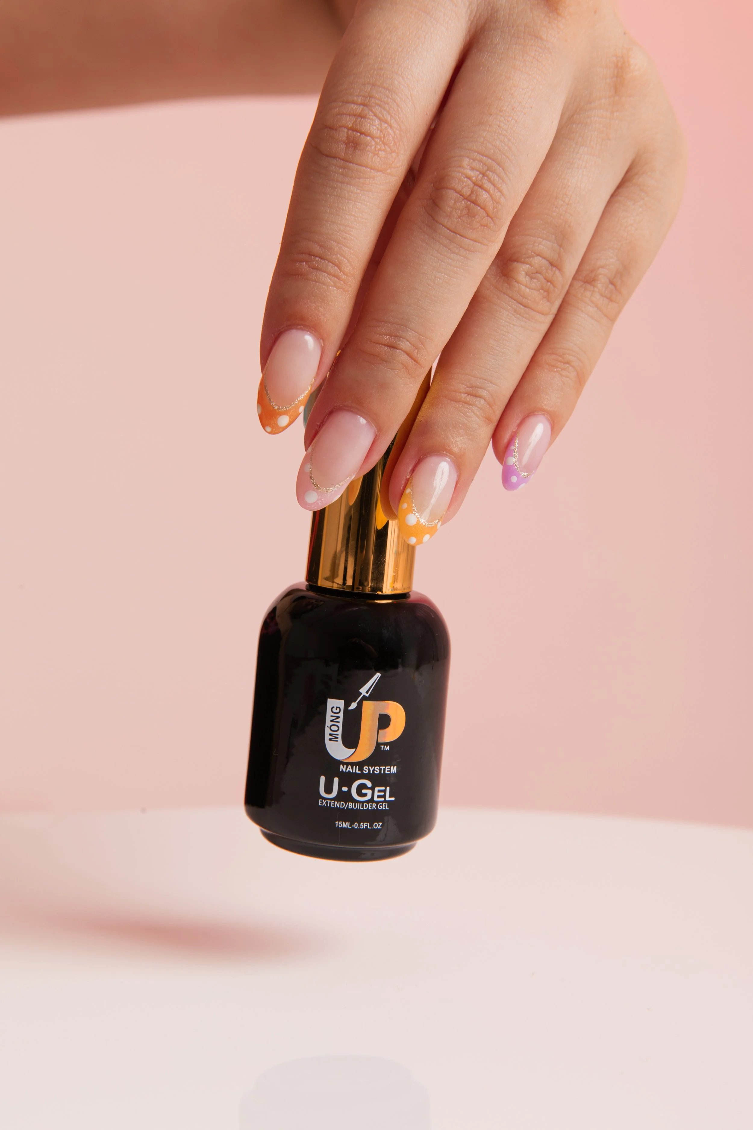 A hand with manicured nails holding a black bottle of U-Gel extend/builder gel over a pink background.