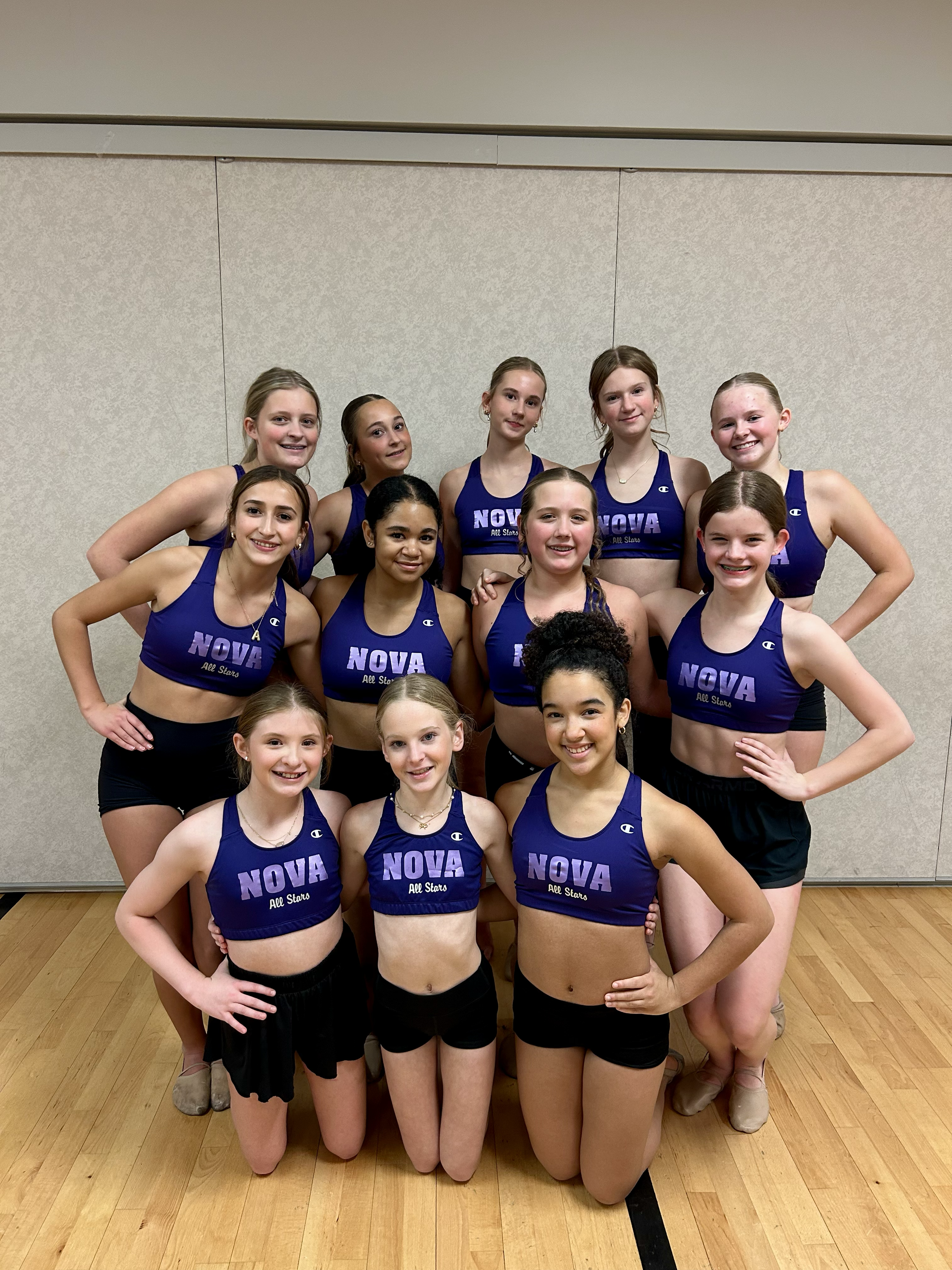 Group of young female cheerleaders in blue and black athletic uniforms posing together indoors.