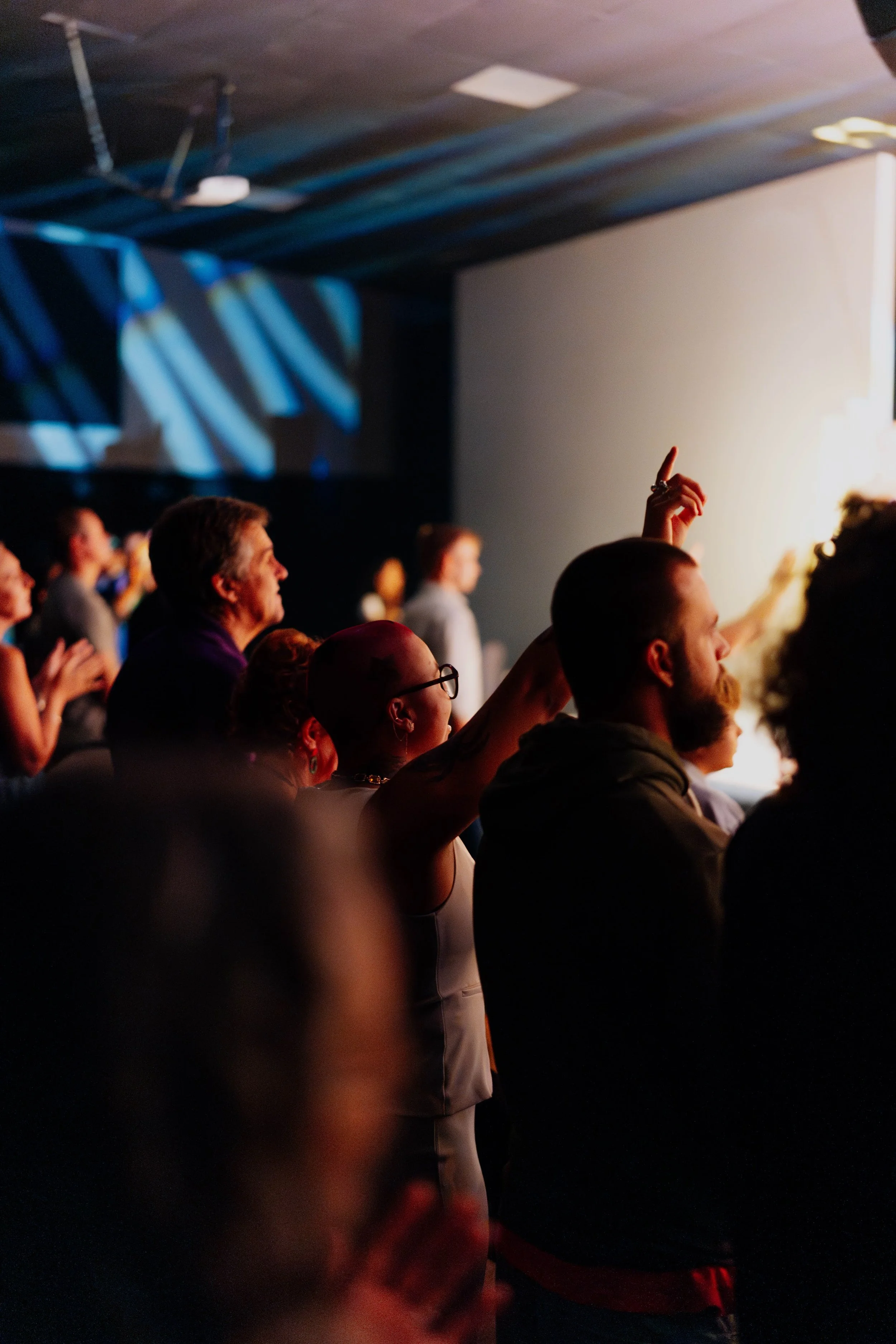 A church praying in a dimly lit room, with one person raising their hand.