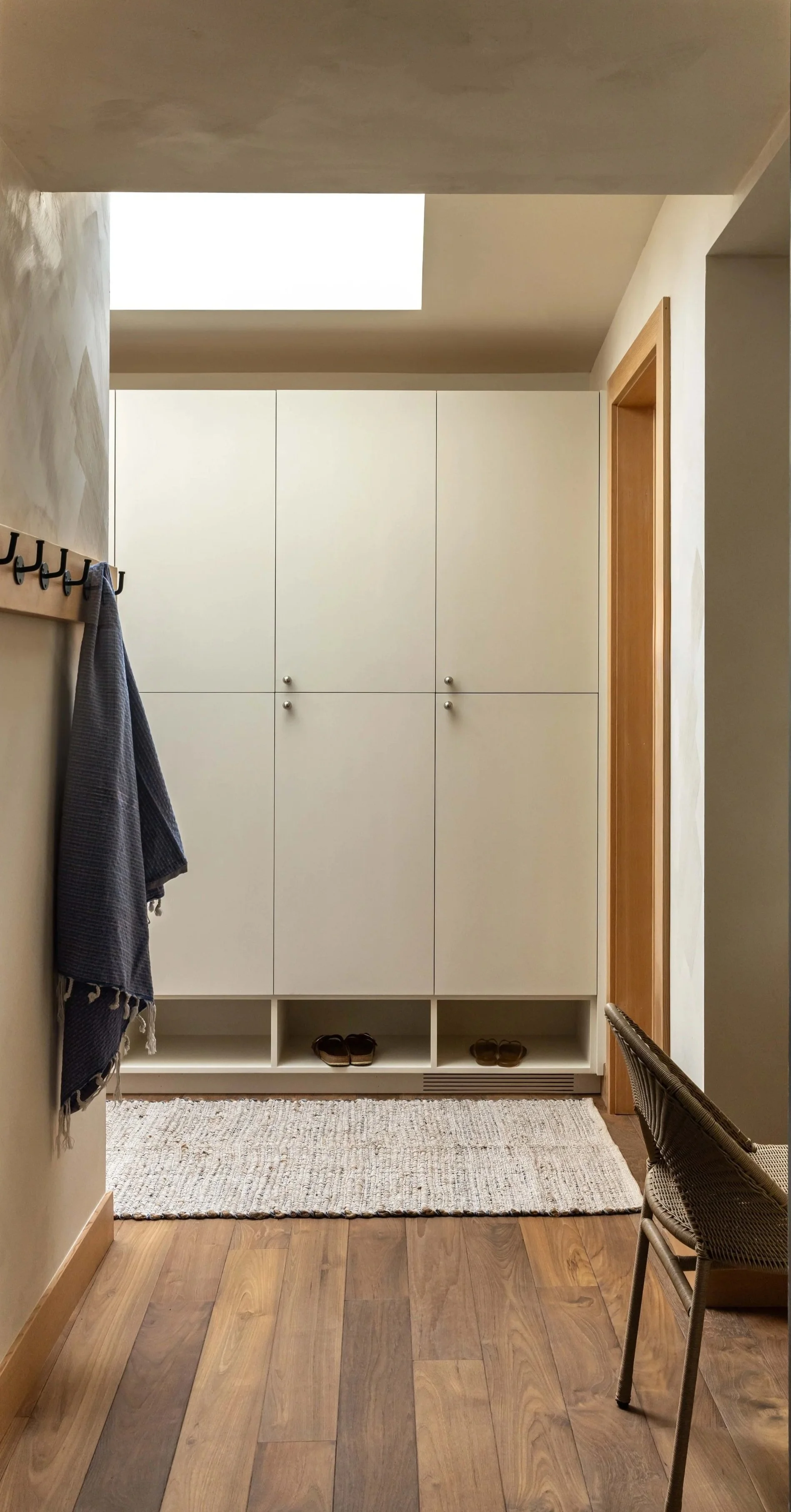 Entryway with a large white storage cabinet, a woven rug, wooden flooring, and a chair.