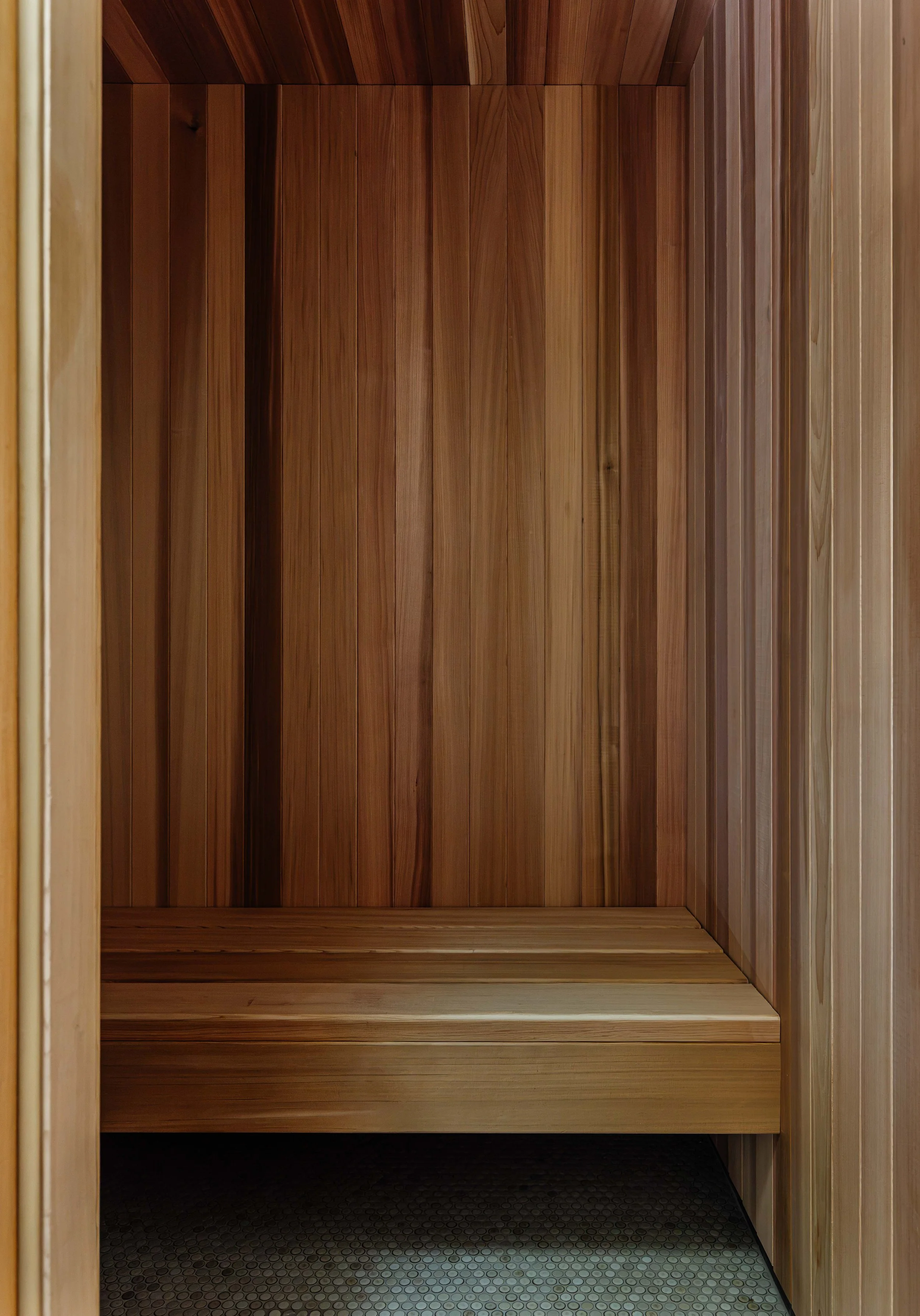 Empty wooden sauna with benches and honeycomb-patterned floor.