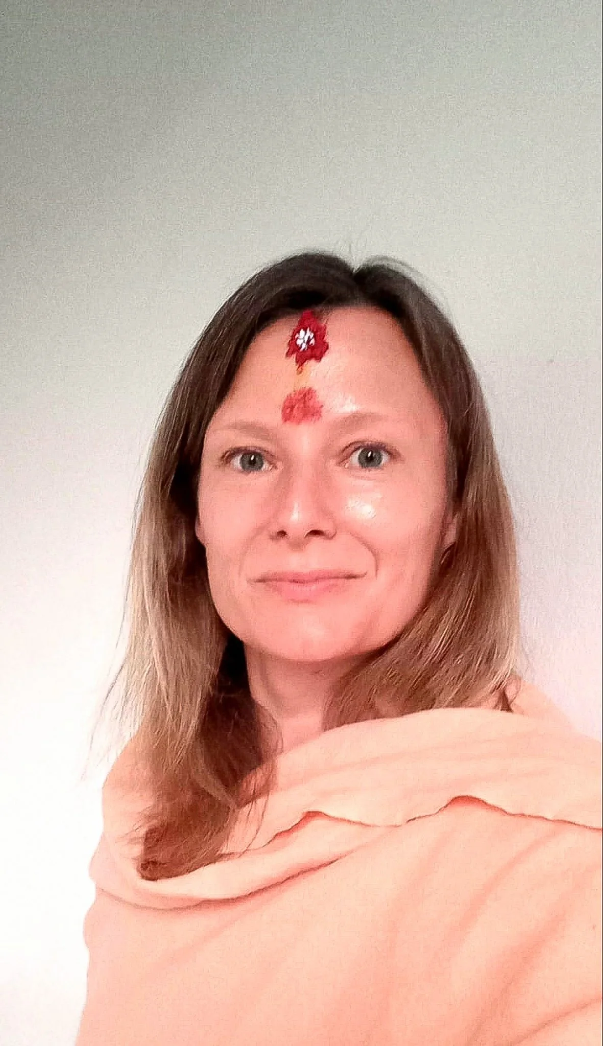Woman with painted red flowers on her forehead, wrapped in a peach-colored shawl.