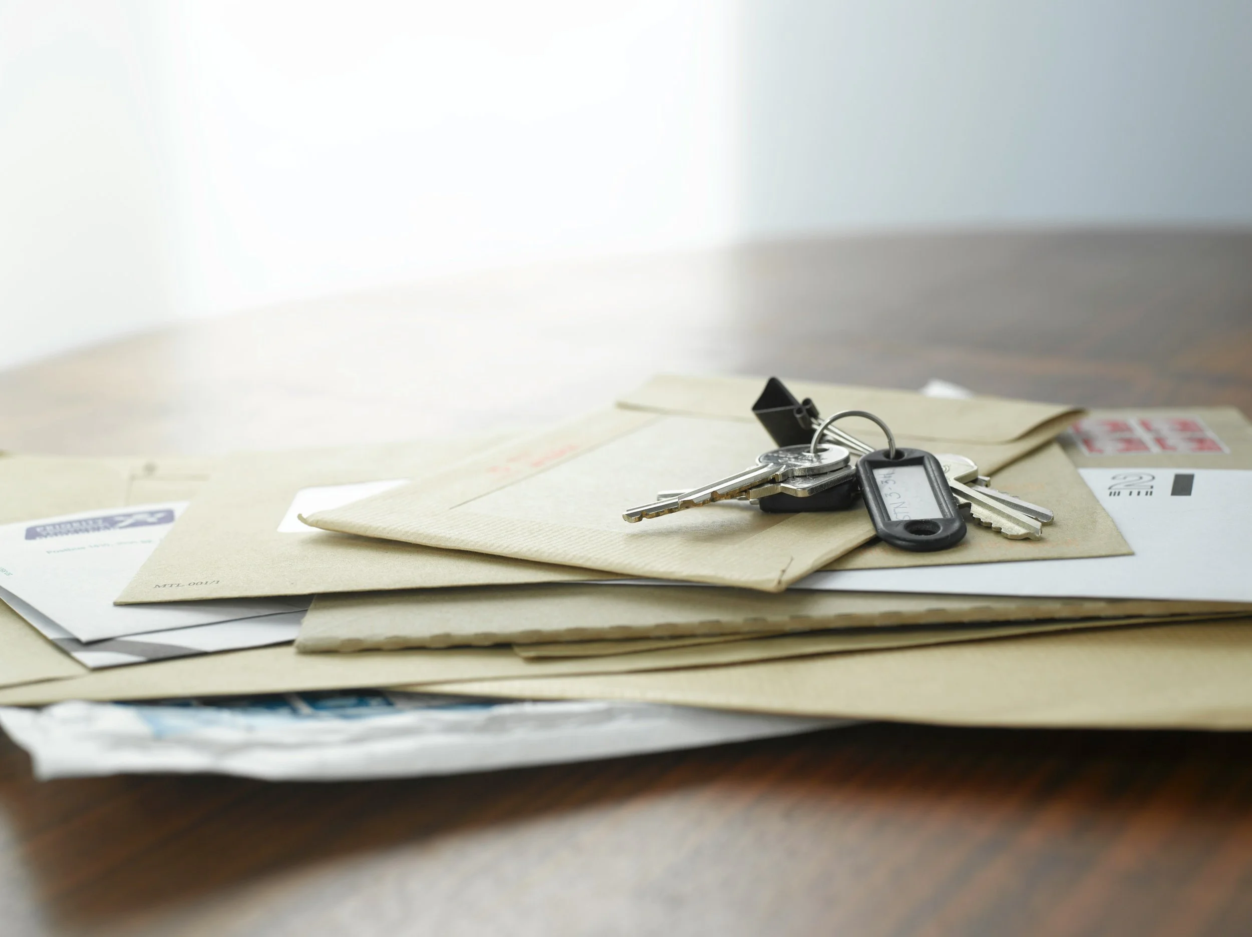 A set of keys on top of envelopes and papers on a wooden table.