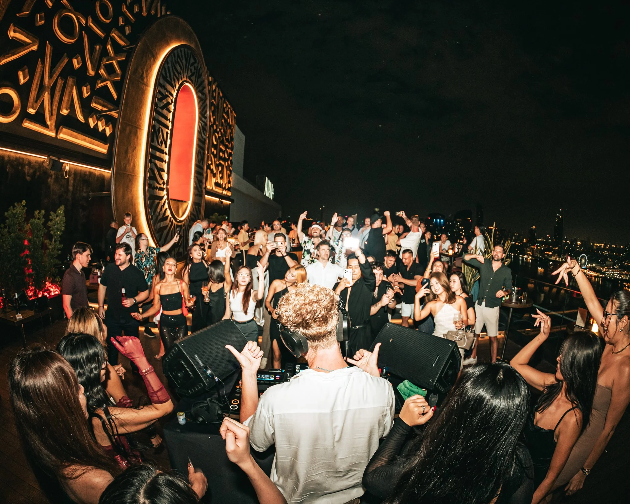 People dancing and socializing at a rooftop party at night, with city lights visible in the background.